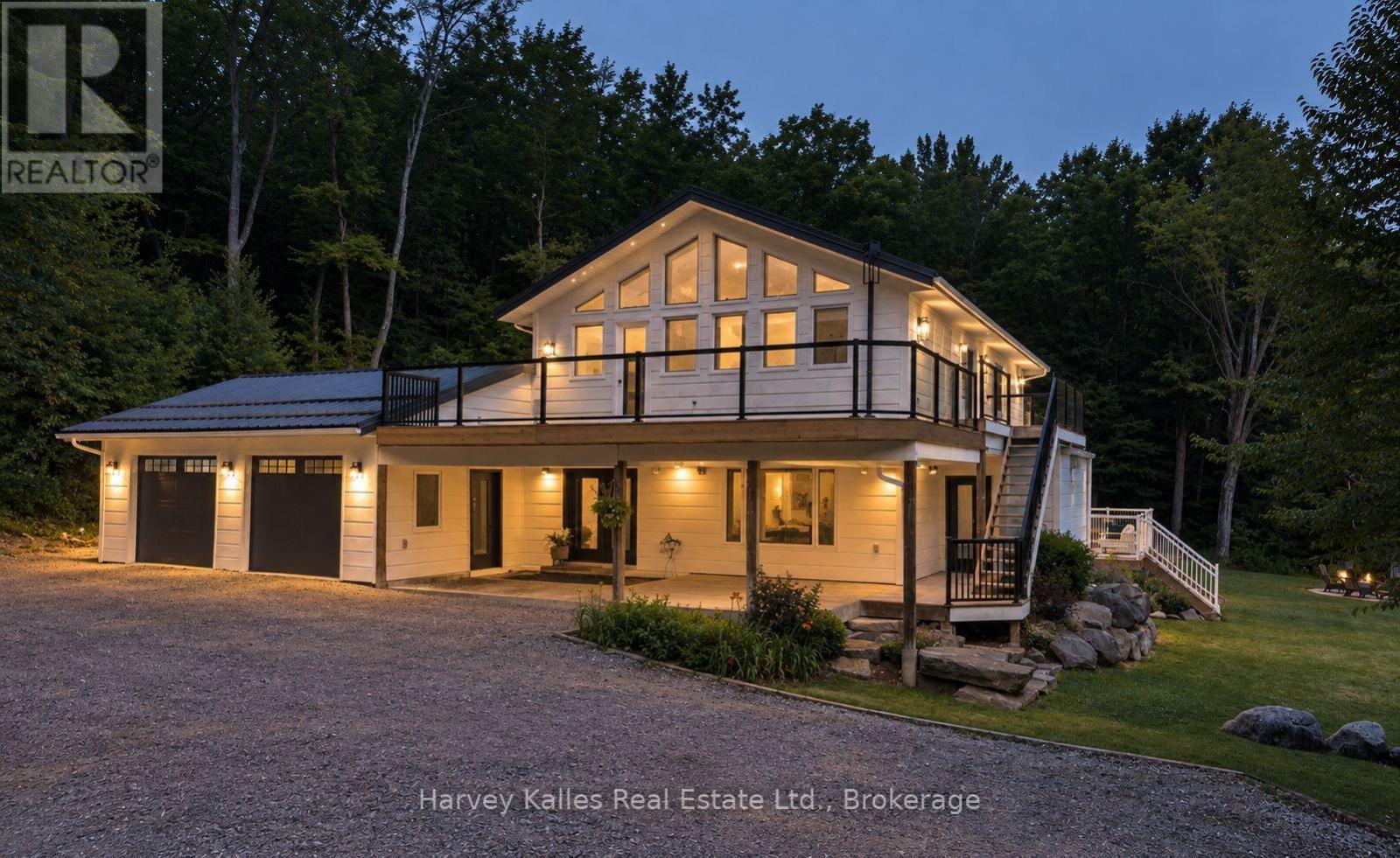Modern white home glowing at dusk, with a raised balcony and double garage among trees.