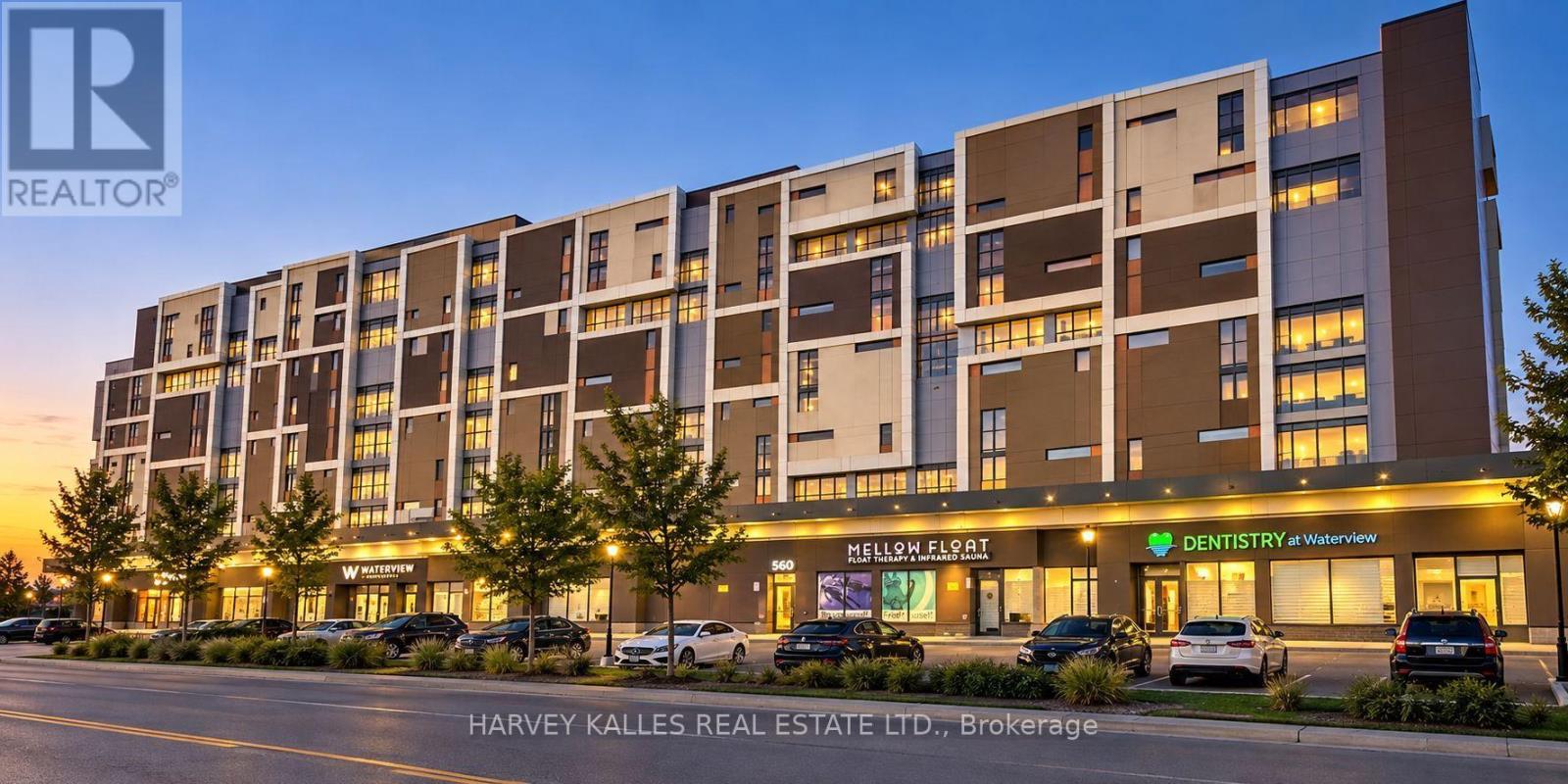 Modern mixed-use mid-rise building with illuminated storefronts and parked cars at dusk.