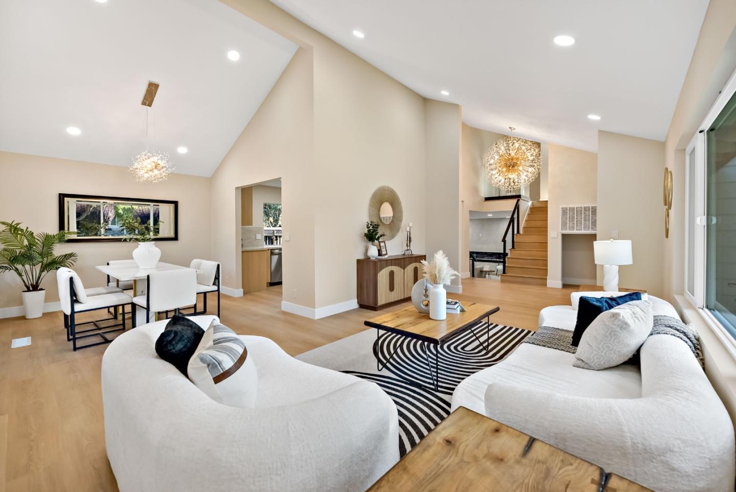 Open-plan living room with white sectional sofas, a patterned rug, and a staircase.