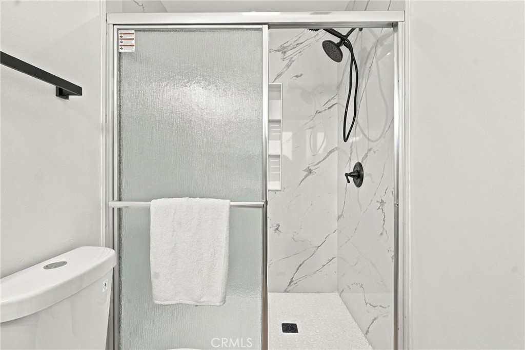 Bathroom shower with marble-look walls, black fixtures, and a sliding frosted-glass door.