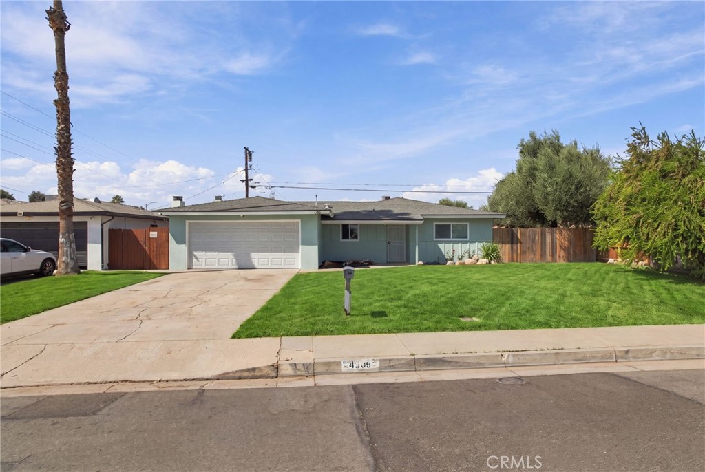 Single-story pale green home with a two-car garage, wide driveway, and neatly mown front lawn.