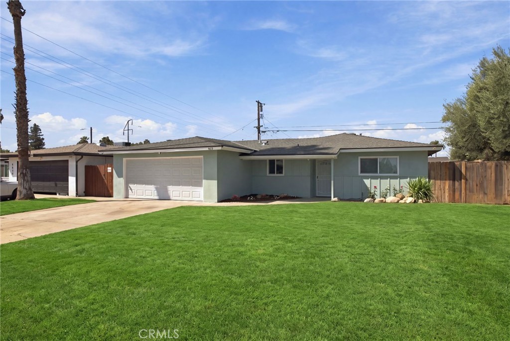 Single-story pale blue house with two garage doors, a broad green lawn, and a concrete driveway.