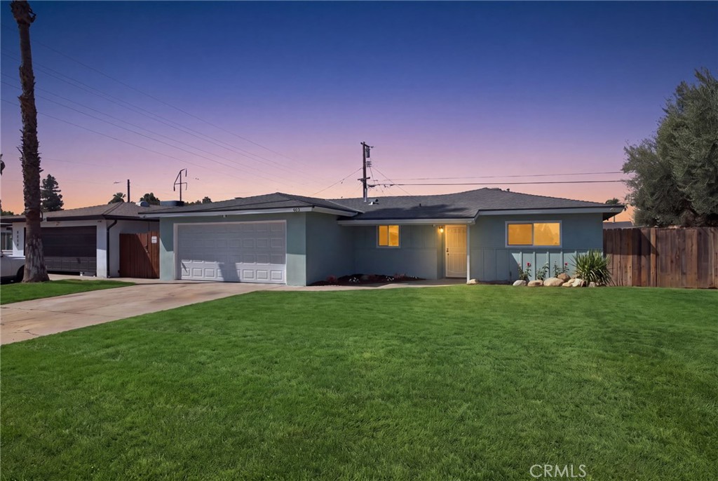 Single-story blue-gray home with an attached garage and broad green lawn at dusk.