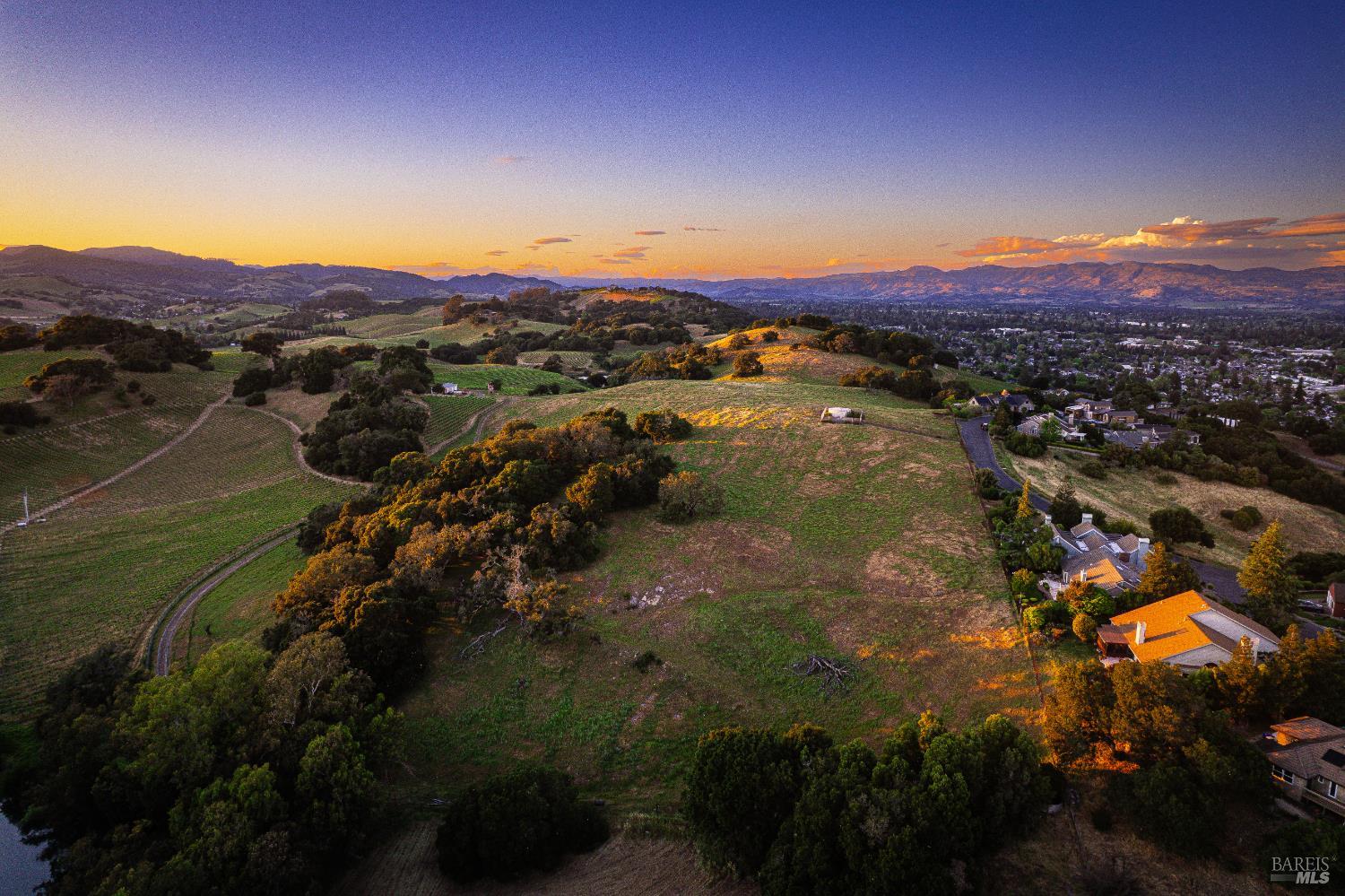 Aerial view of rolling vineyard land and scattered homes in warm sunset light.