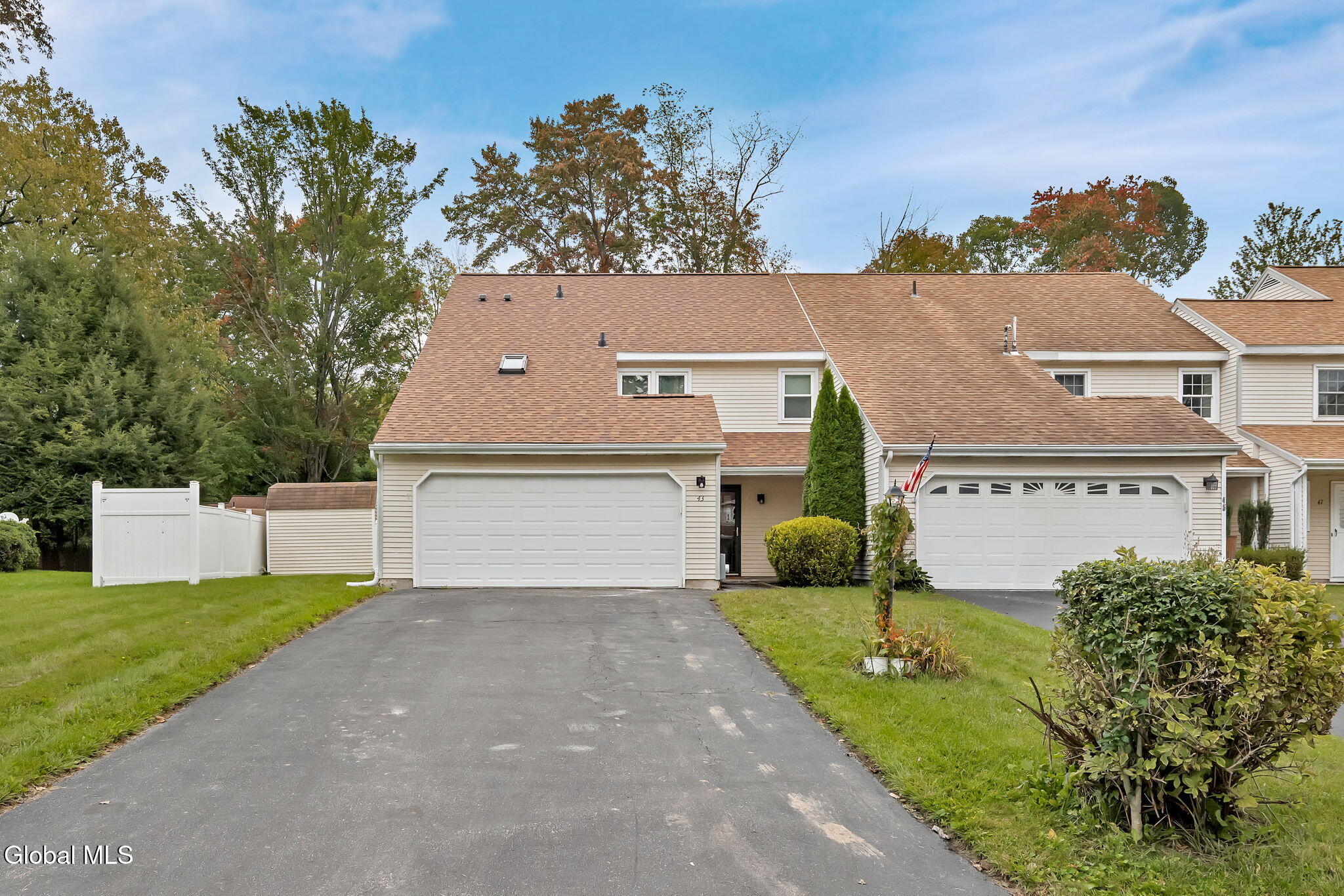 Attached beige homes with white garage doors, wide driveways, and autumn trees.