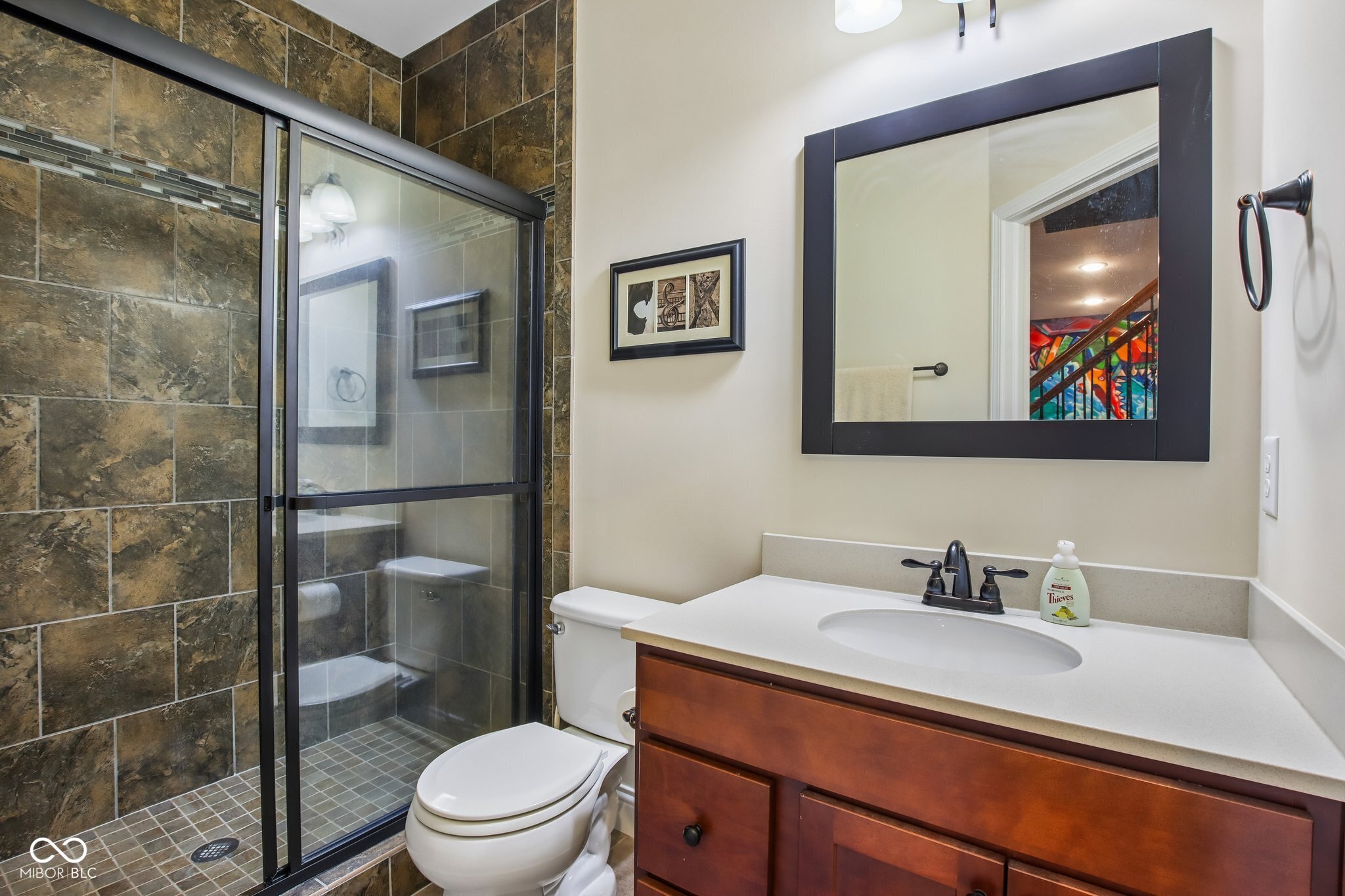 Bathroom with a brown-tiled glass shower, white toilet, and dark wood vanity.