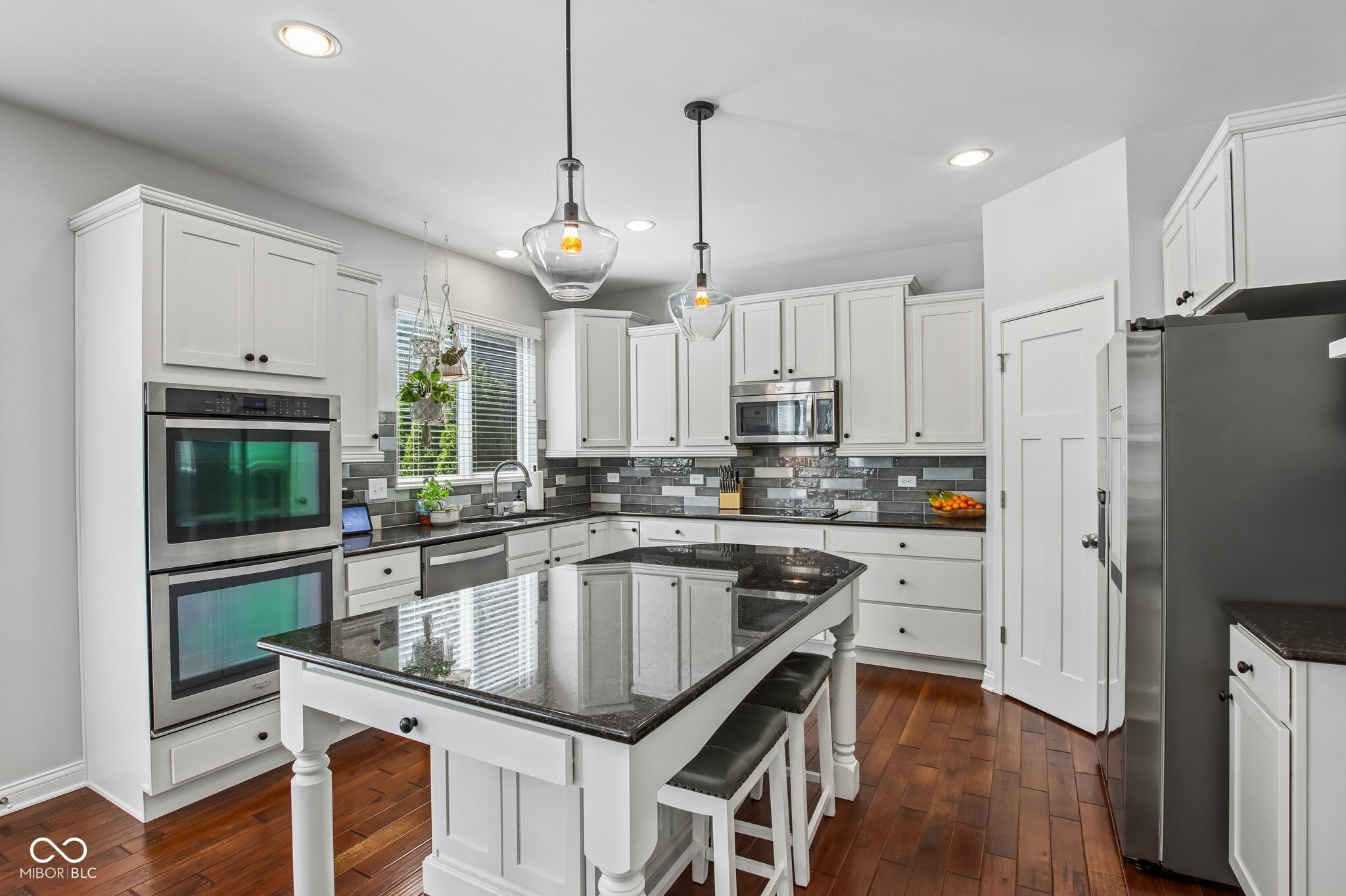 Bright kitchen with white cabinets, dark granite island, stainless steel appliances, and hardwood floors.