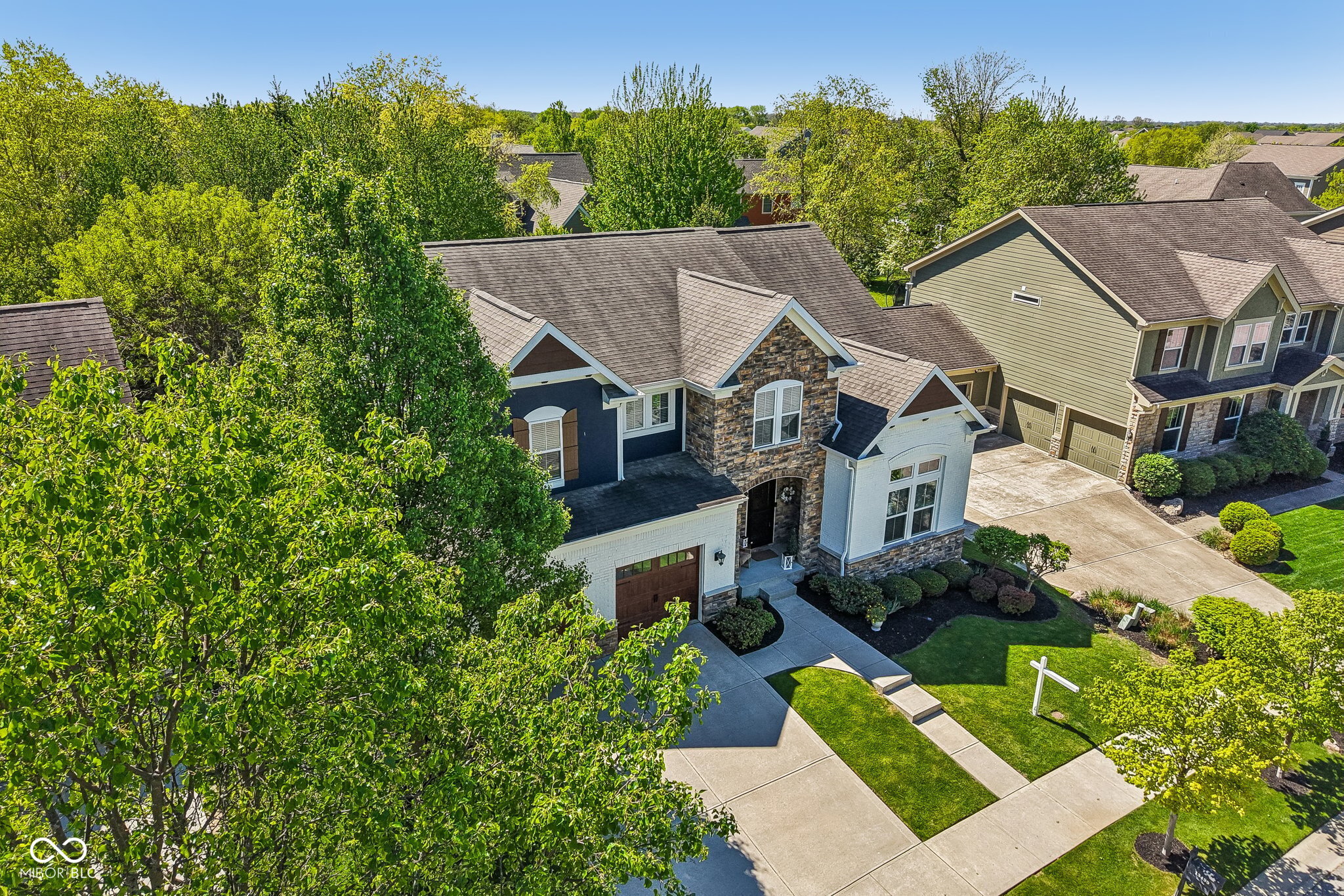 Aerial view of a two-story home with a stone facade, attached garage, and landscaped front lawn.