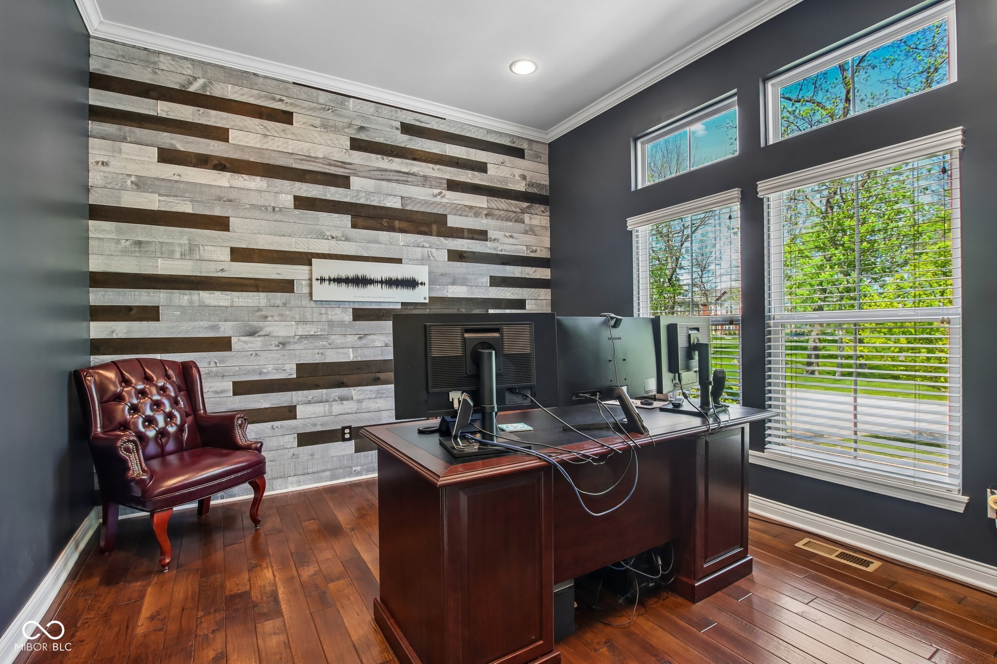 Home office with a multi-monitor desk, burgundy leather chair, and reclaimed-wood accent wall.