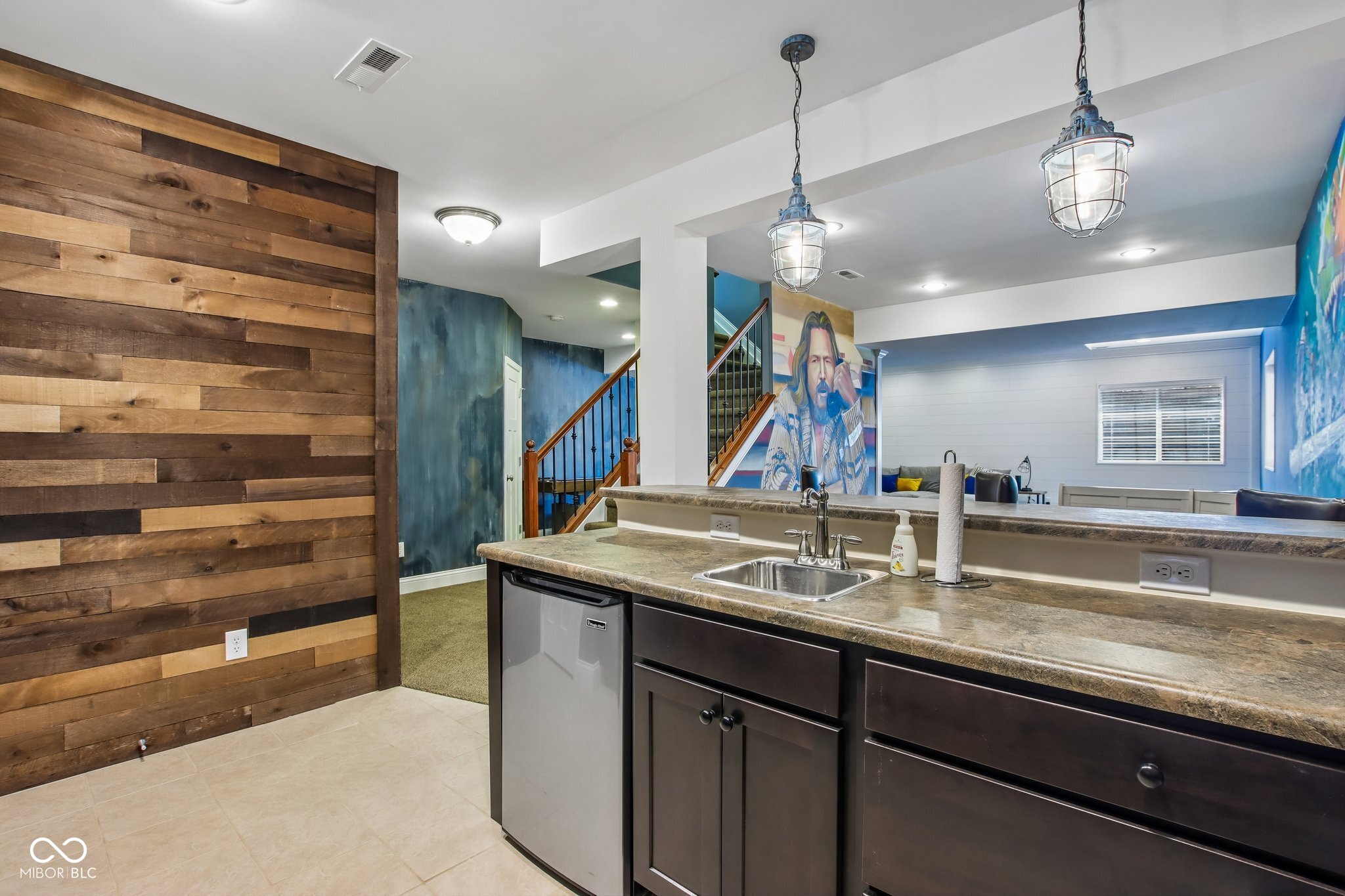 Finished lower-level kitchenette with granite counter, sink, mini fridge, and wood-plank accent wall.