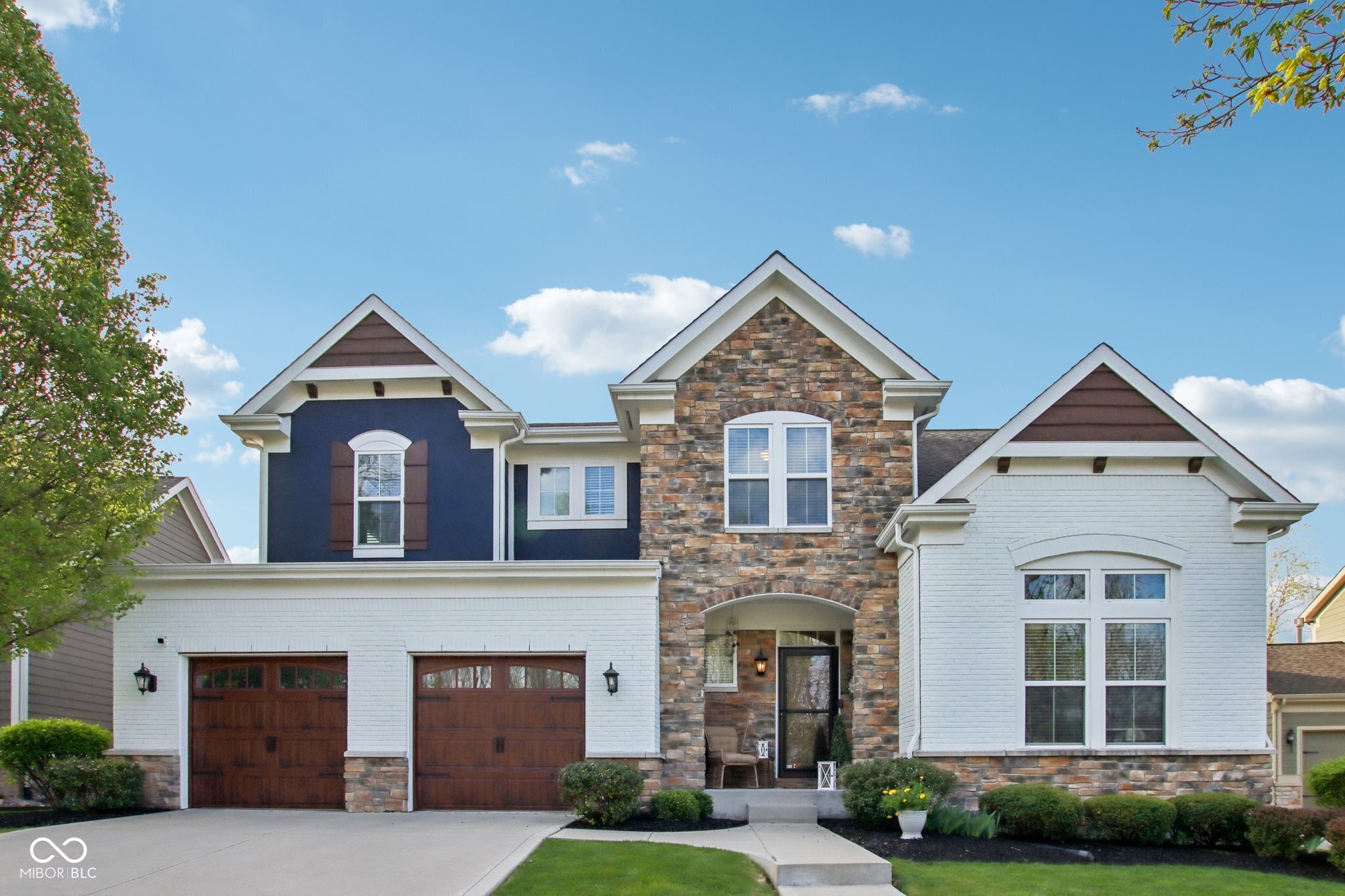 Two-story home with a stone facade, white brick wings, and two brown garage doors.