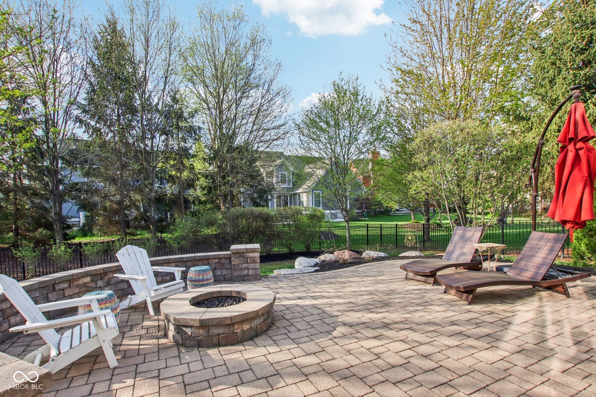 Backyard patio with a stone fire pit, Adirondack chairs, chaise lounges, and a red umbrella.