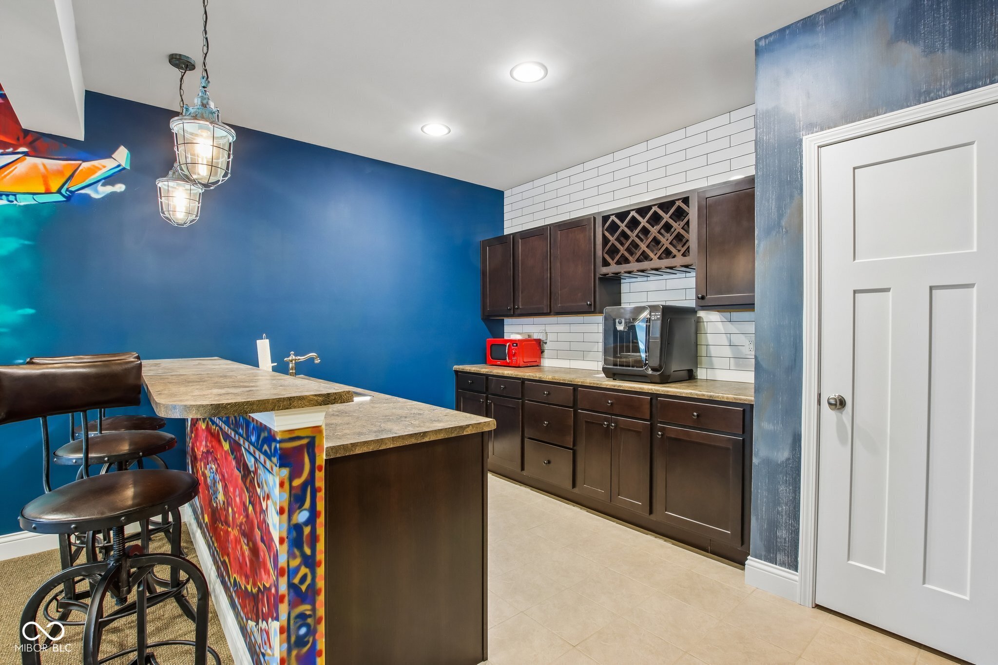 Kitchen with dark cabinets, white subway tile, a colorful island, and bar stools.