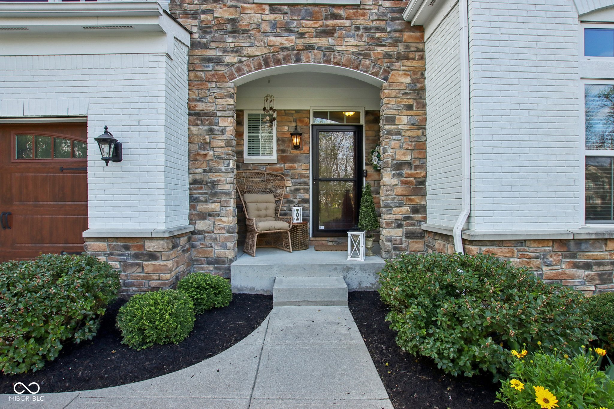 Home entrance with a stone archway, wicker chair, and landscaped walkway.