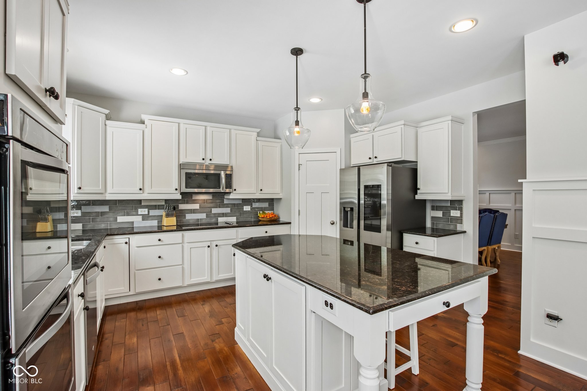 Kitchen with white cabinets, stainless steel appliances, gray tile backsplash, and a large dark-stone island.