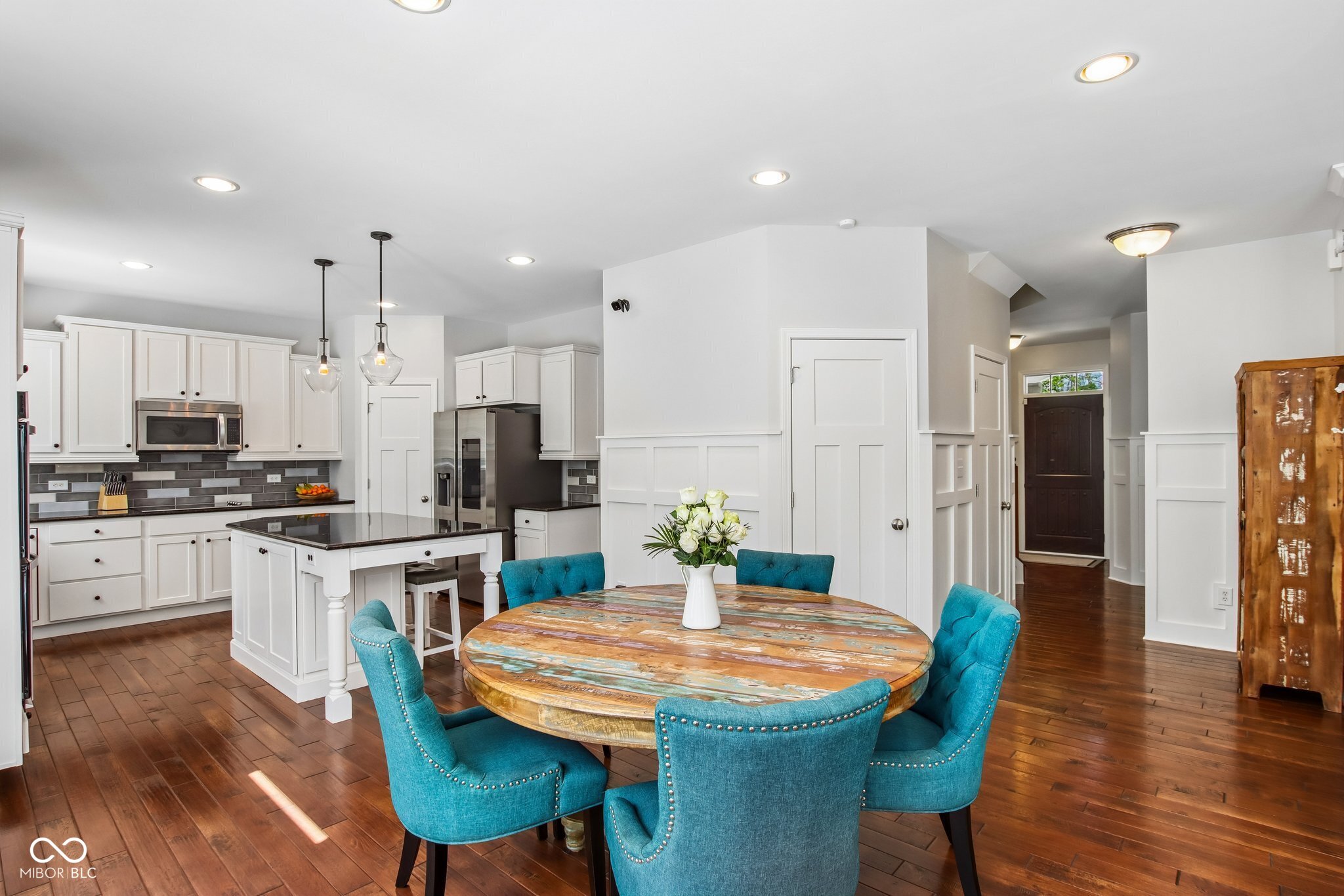 Kitchen and dining area with white cabinetry, a rustic round table, and teal chairs.