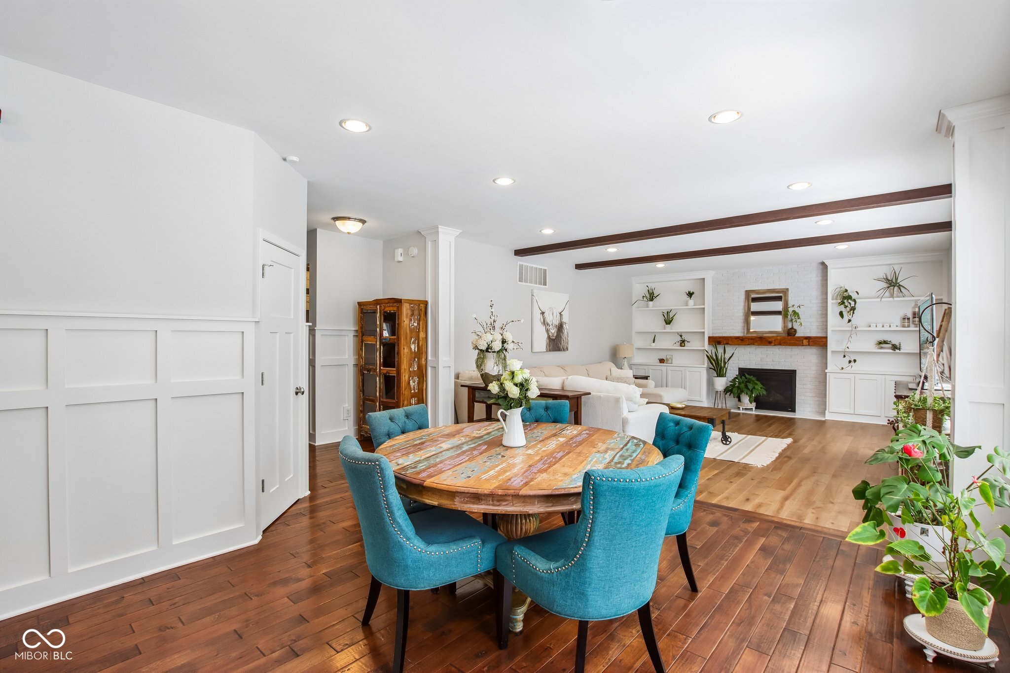 Open dining and living room with round table, blue chairs, and white brick fireplace.