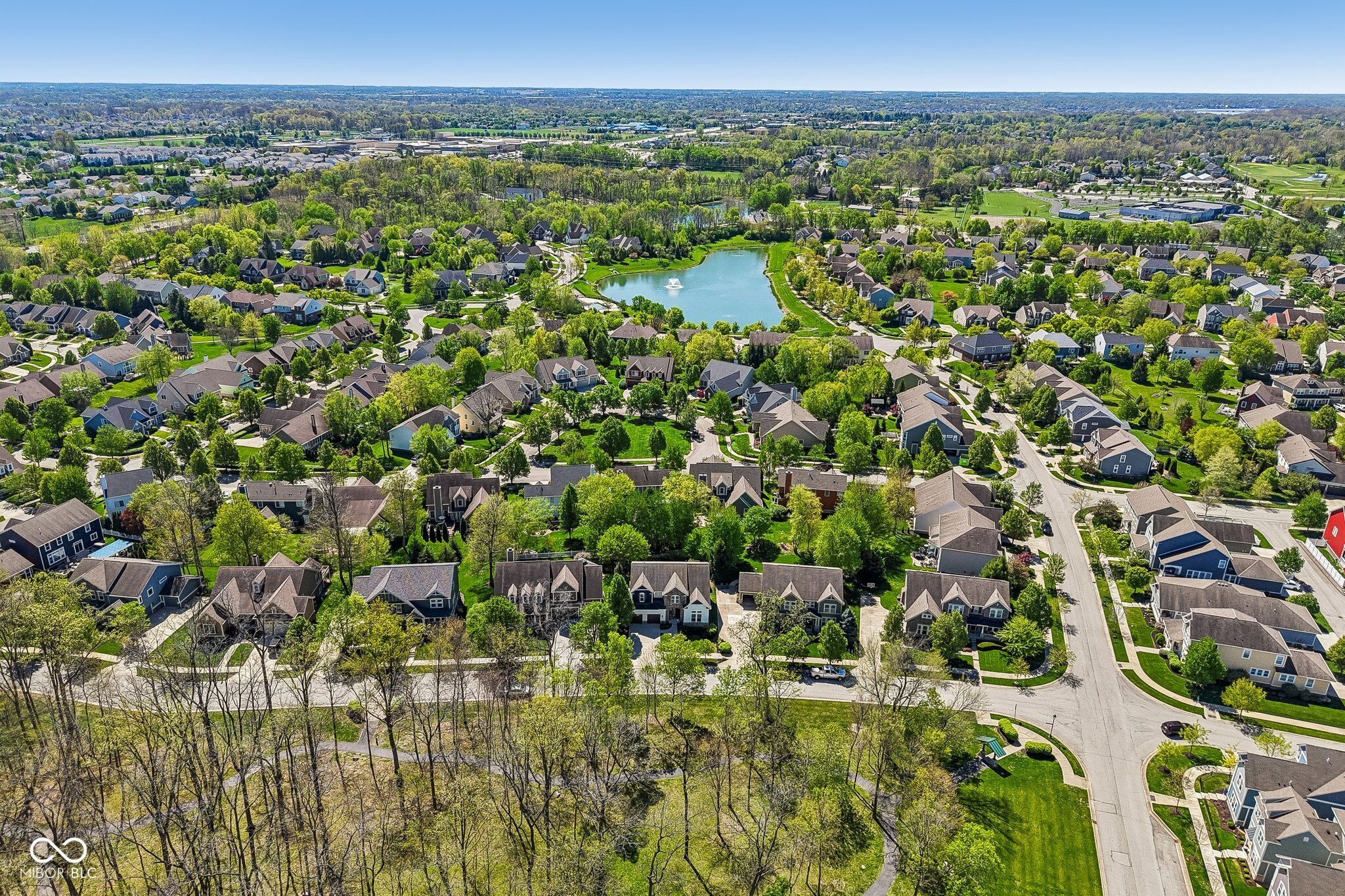 Aerial view of a suburban neighborhood with a pond, fountain, and wooded green space.