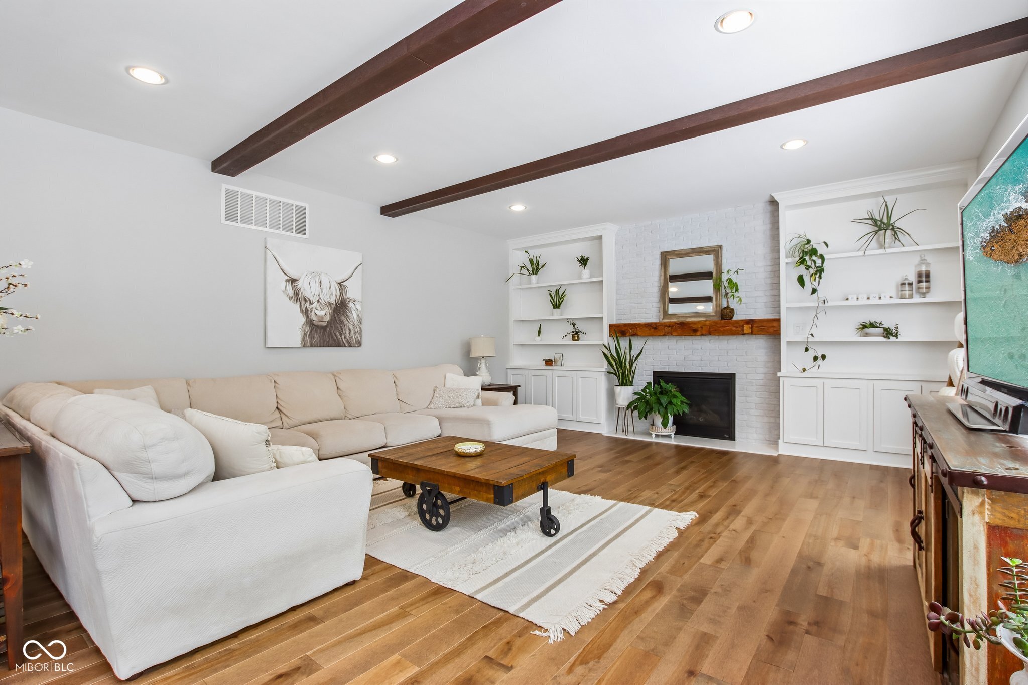 Staged living room with a white brick fireplace, built-in shelves, and exposed ceiling beams.