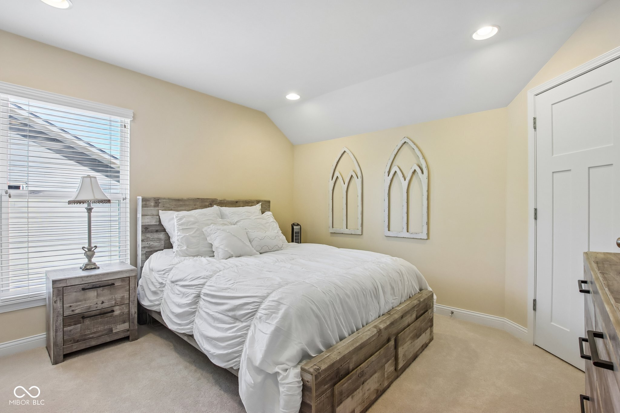 Bedroom with white bedding, a rustic wood bed frame, and arched wall decor.