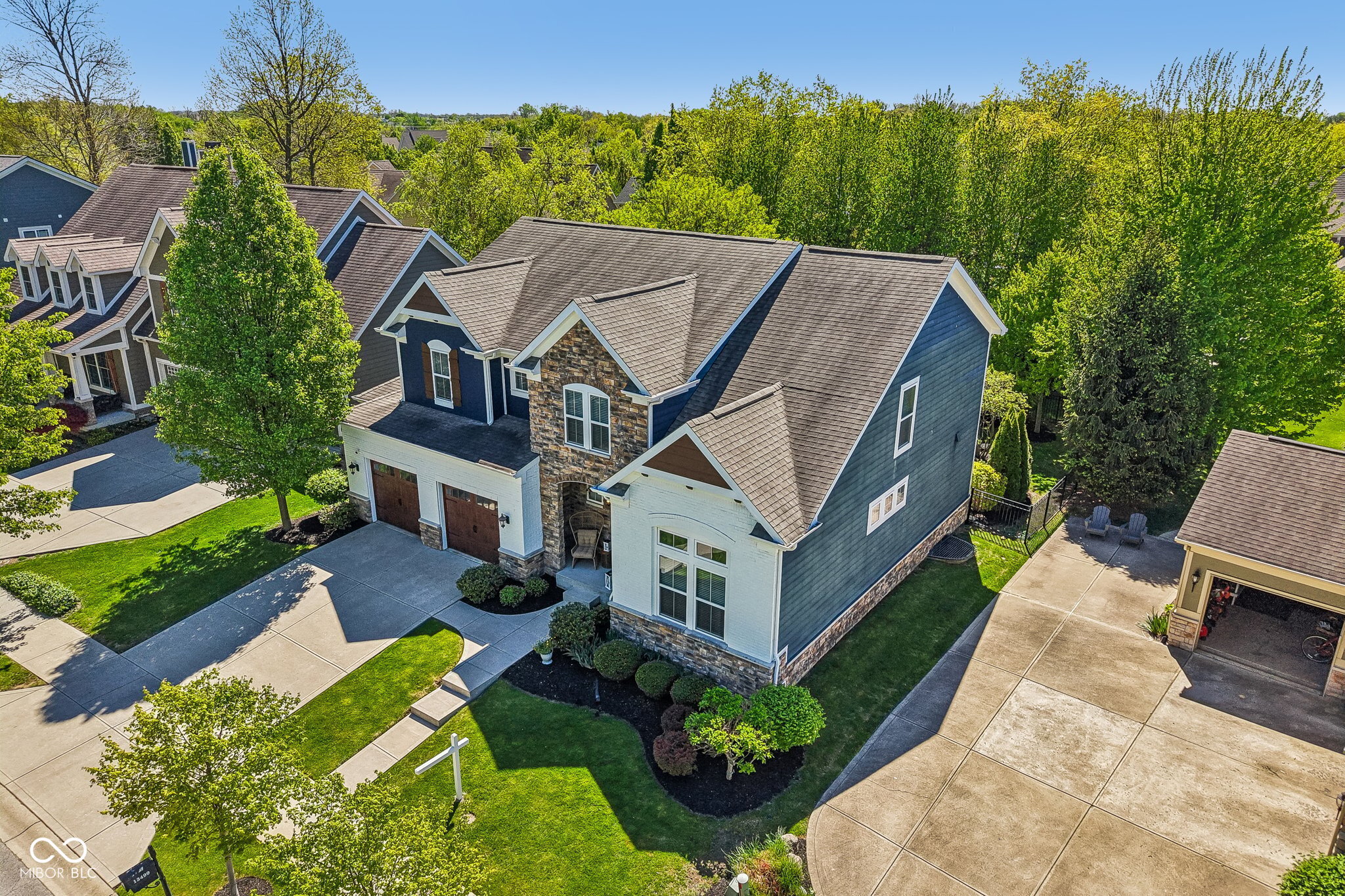 Aerial view of a blue-and-white two-story home with stone accents, a double garage, and landscaped yard.