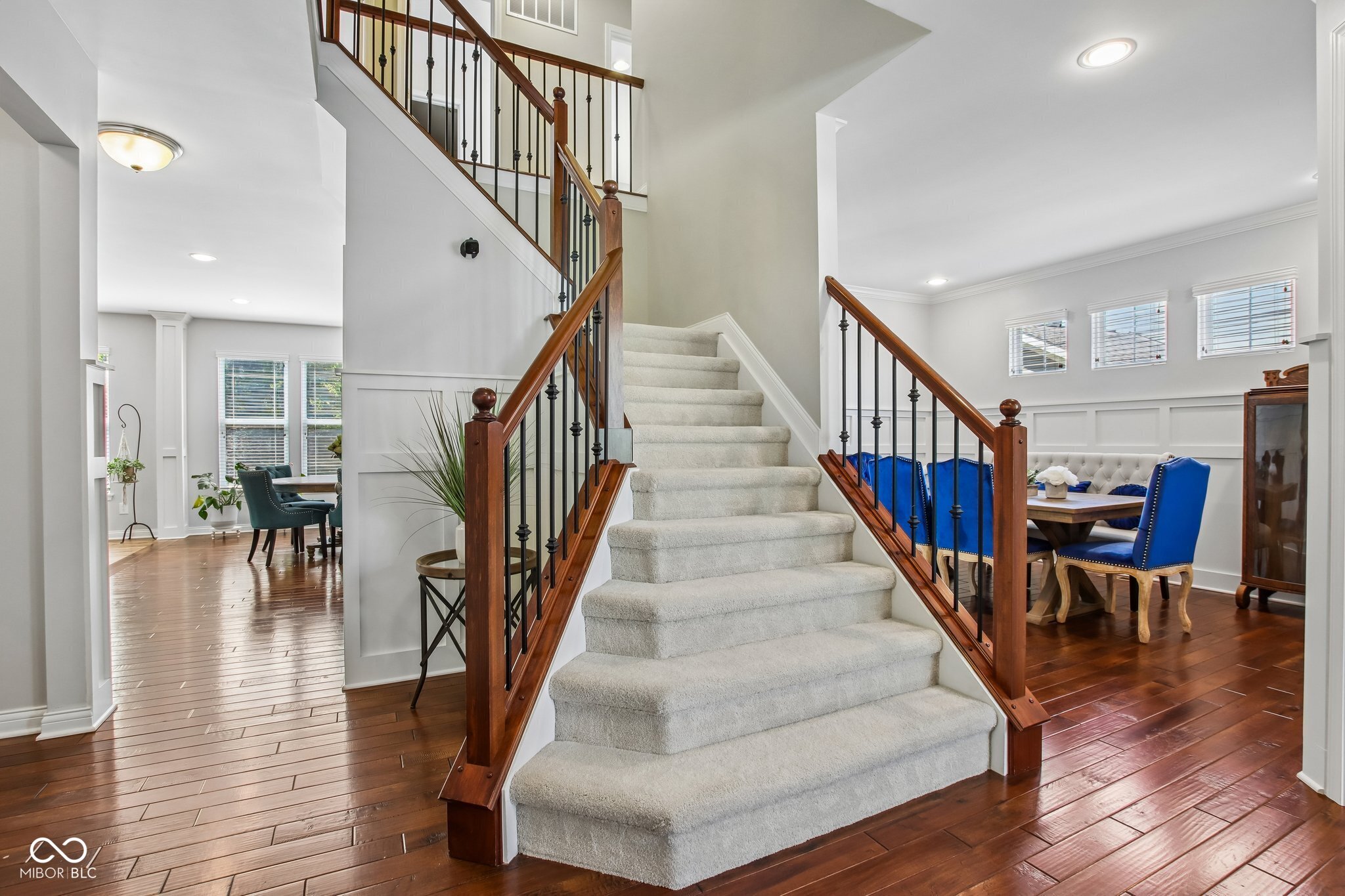 Carpeted staircase with dark wood railings between two dining areas with hardwood floors.