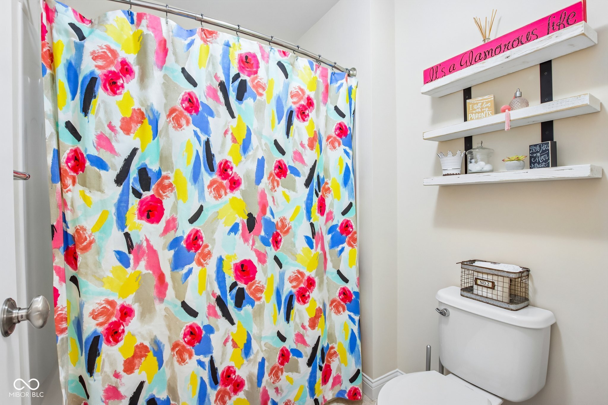 Bathroom with a colorful floral shower curtain, white floating shelves, and a toilet.