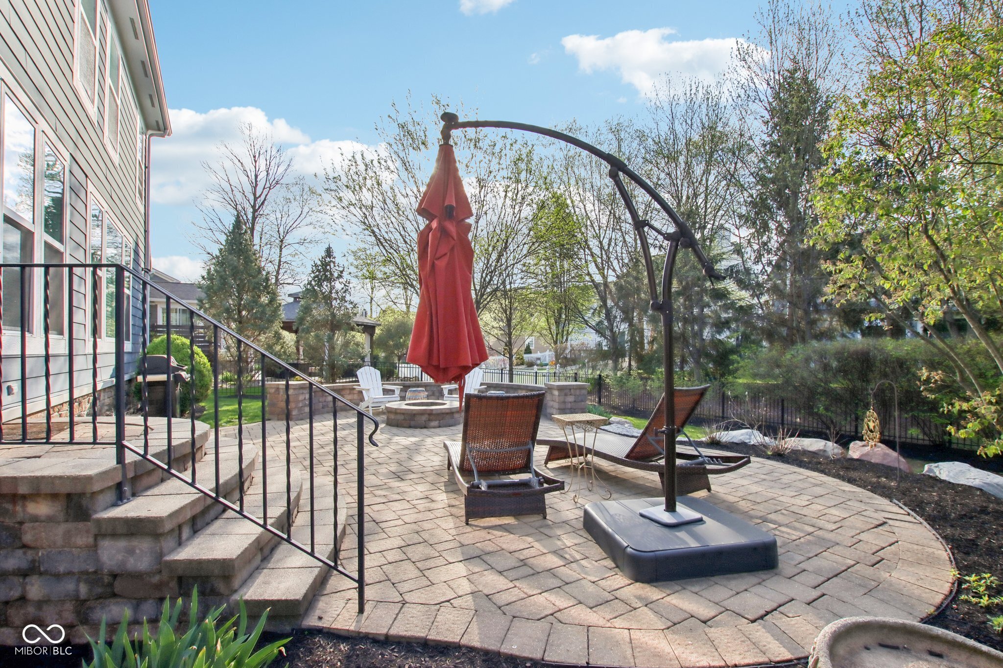 Backyard patio with a stone fire pit, lounge chairs, and a red umbrella beside the house.