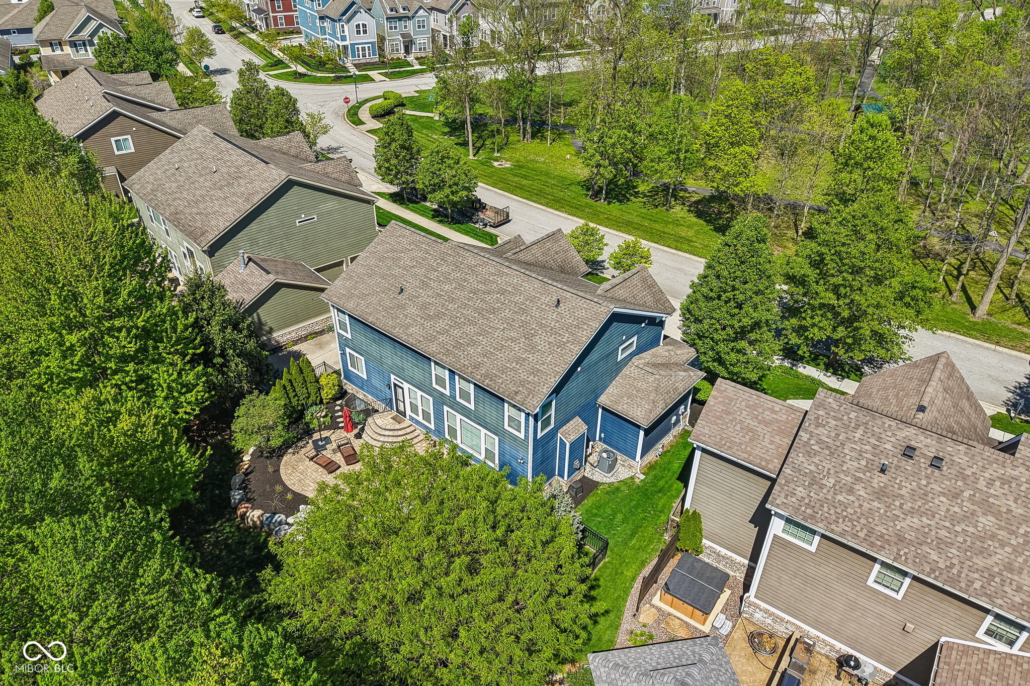 Aerial view of a blue two-story home with a curved stone patio and mature trees.