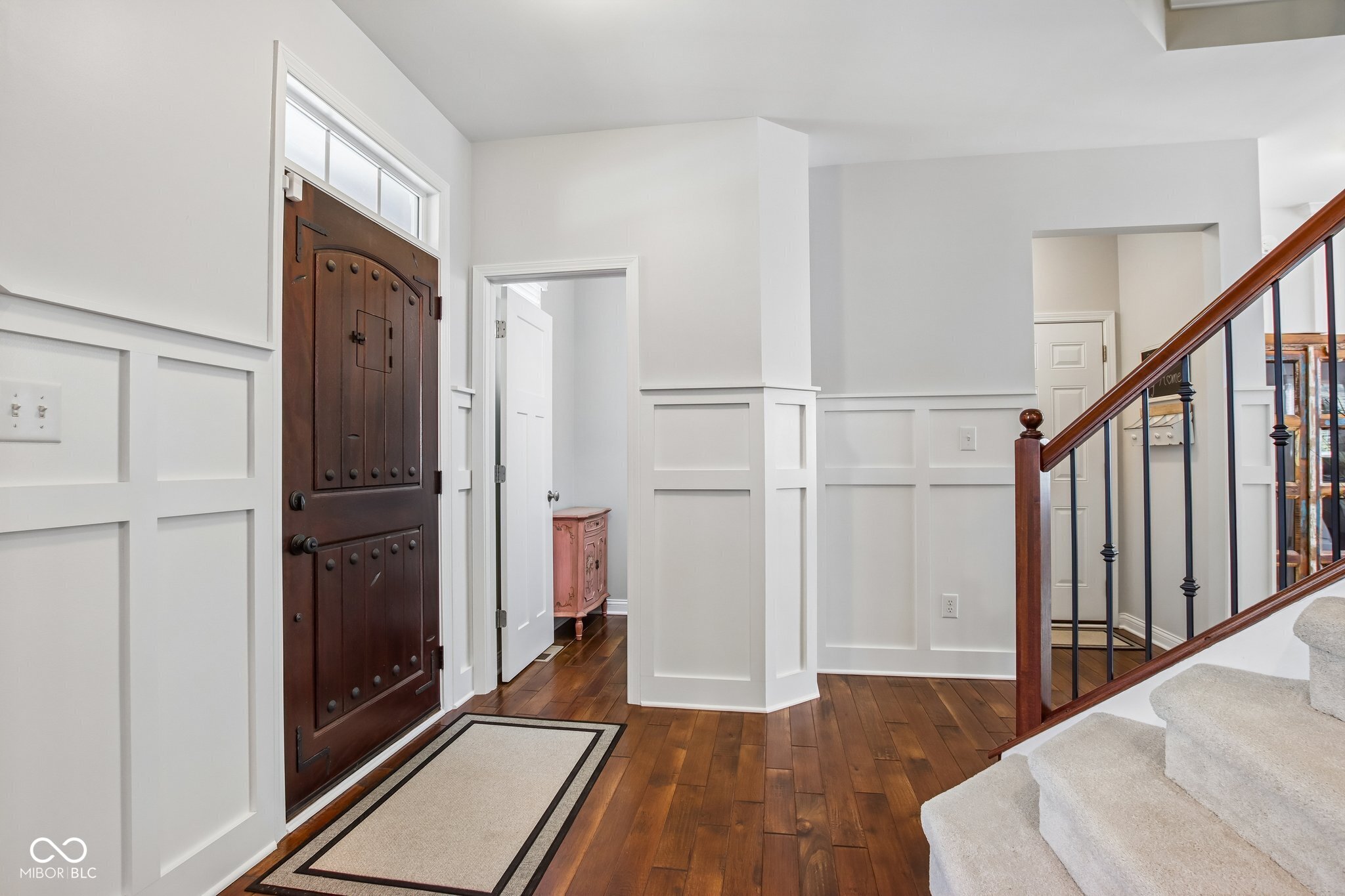 Entry foyer with a dark wood front door, hardwood floors, paneled walls, and a carpeted staircase.