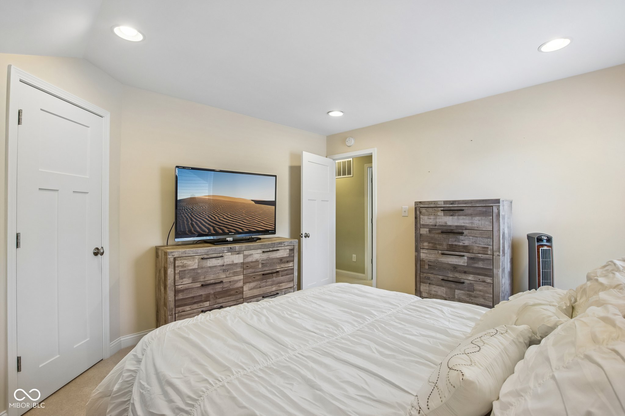 Bedroom with a white bed, rustic wood dressers, and a television.