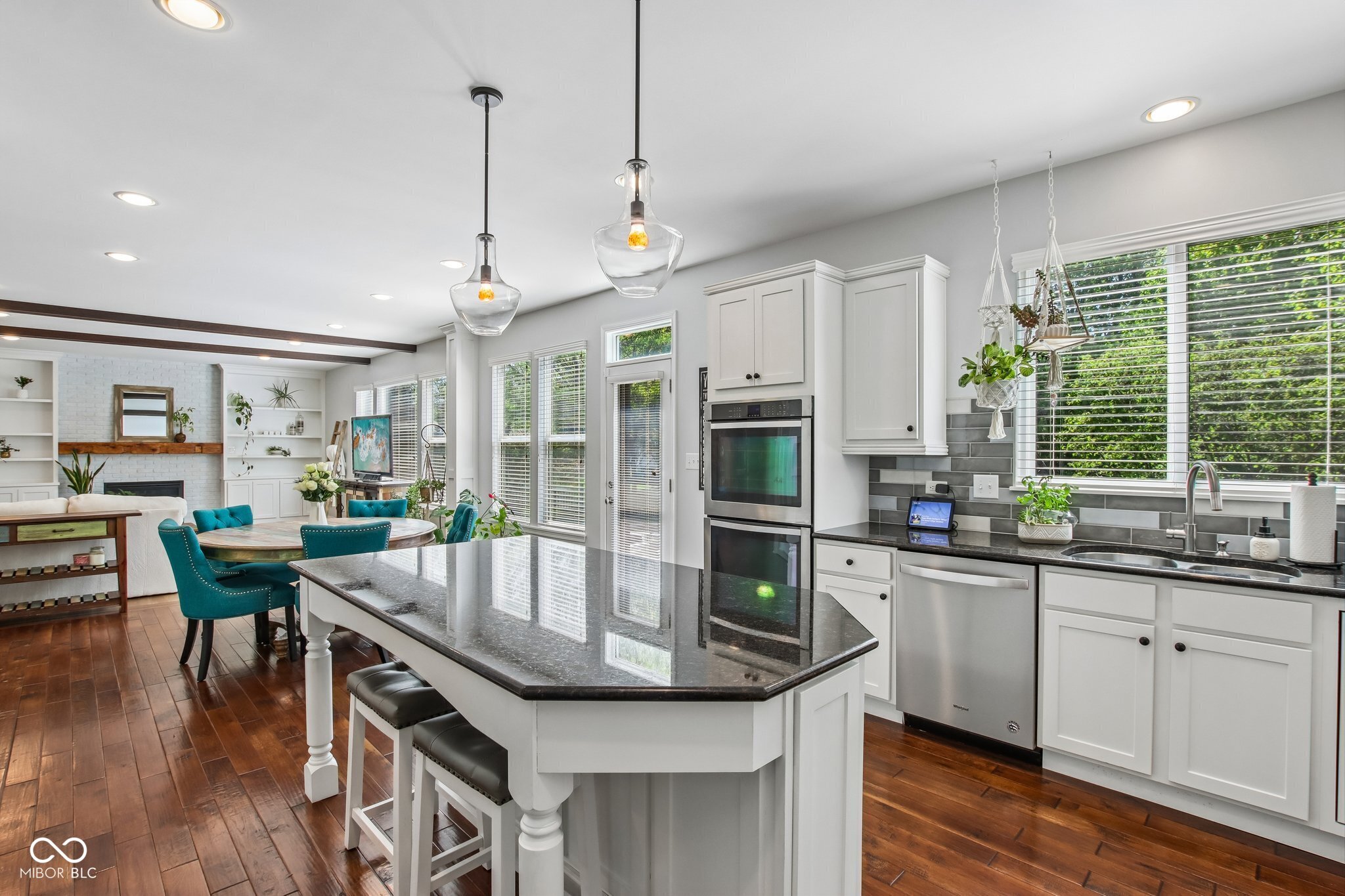 Kitchen with a large dark stone island, white cabinetry, and double wall ovens beside the dining area.