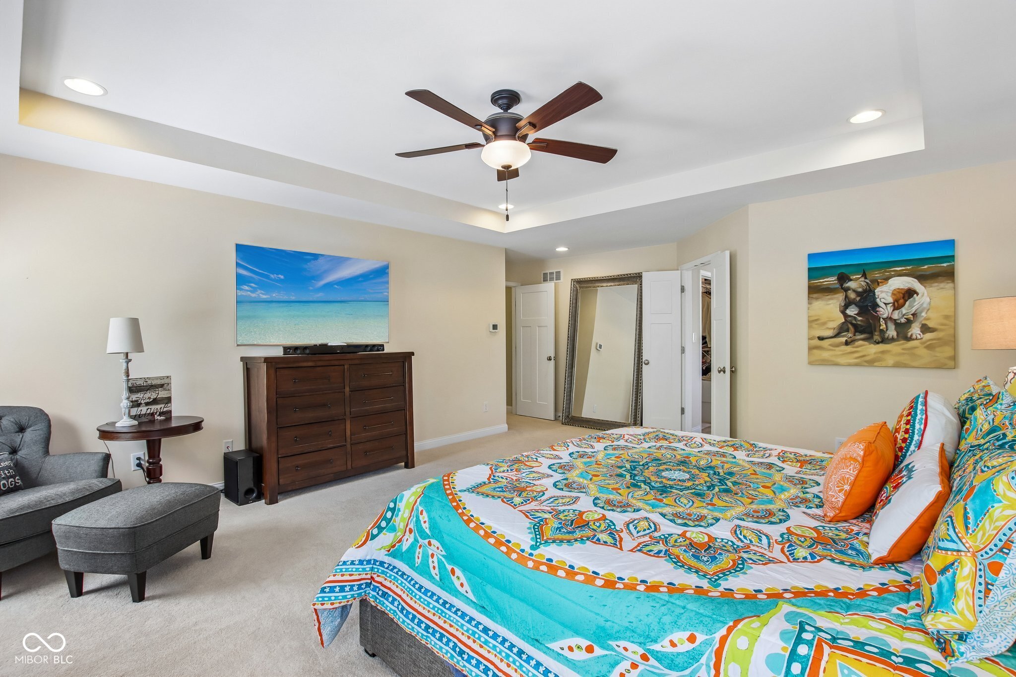 Furnished bedroom with a colorful patterned bedspread, dark wood dresser, and ceiling fan.