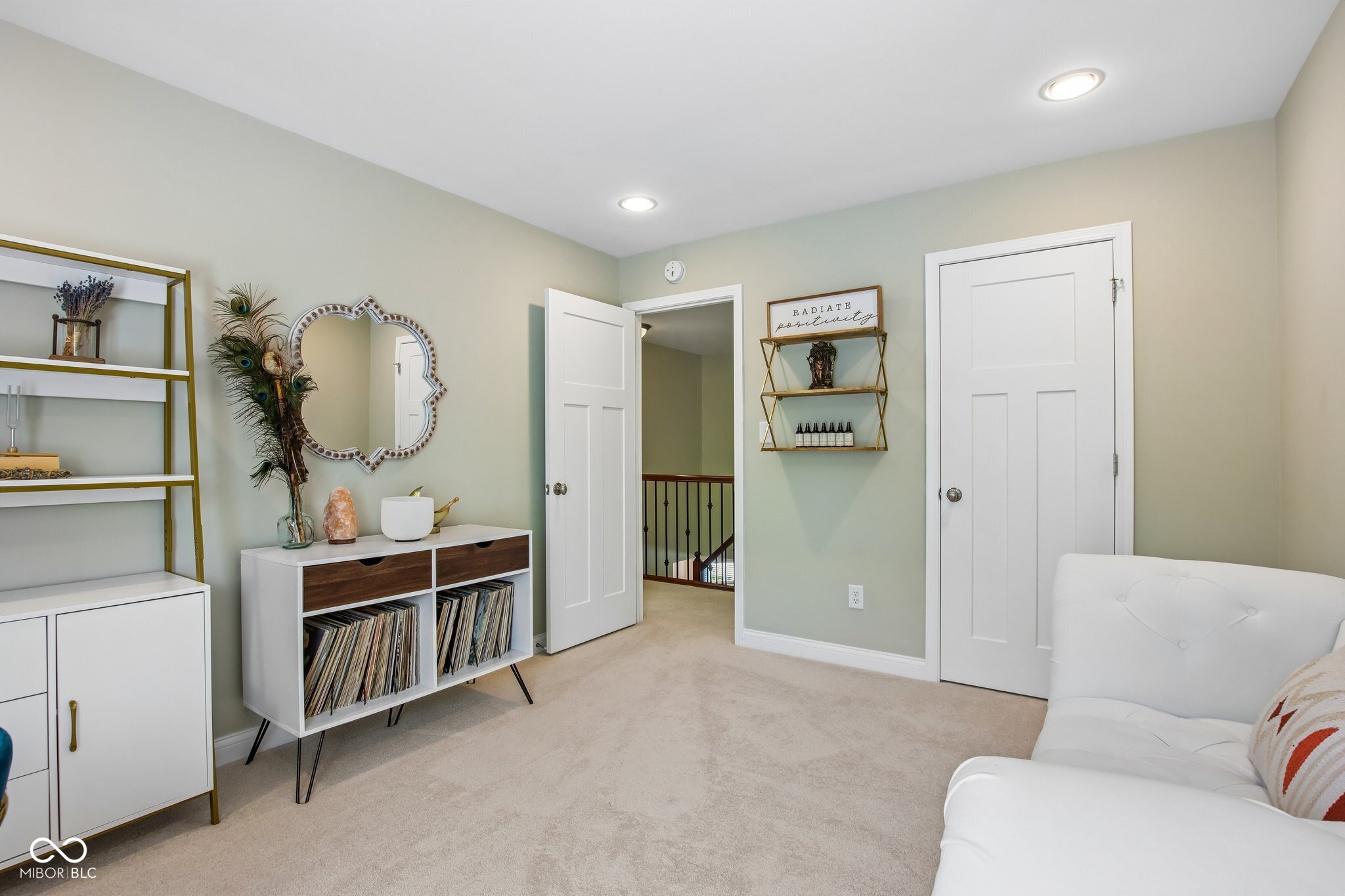 Carpeted sitting room with a white sofa, vinyl record cabinet, and open doorway to a railed landing.