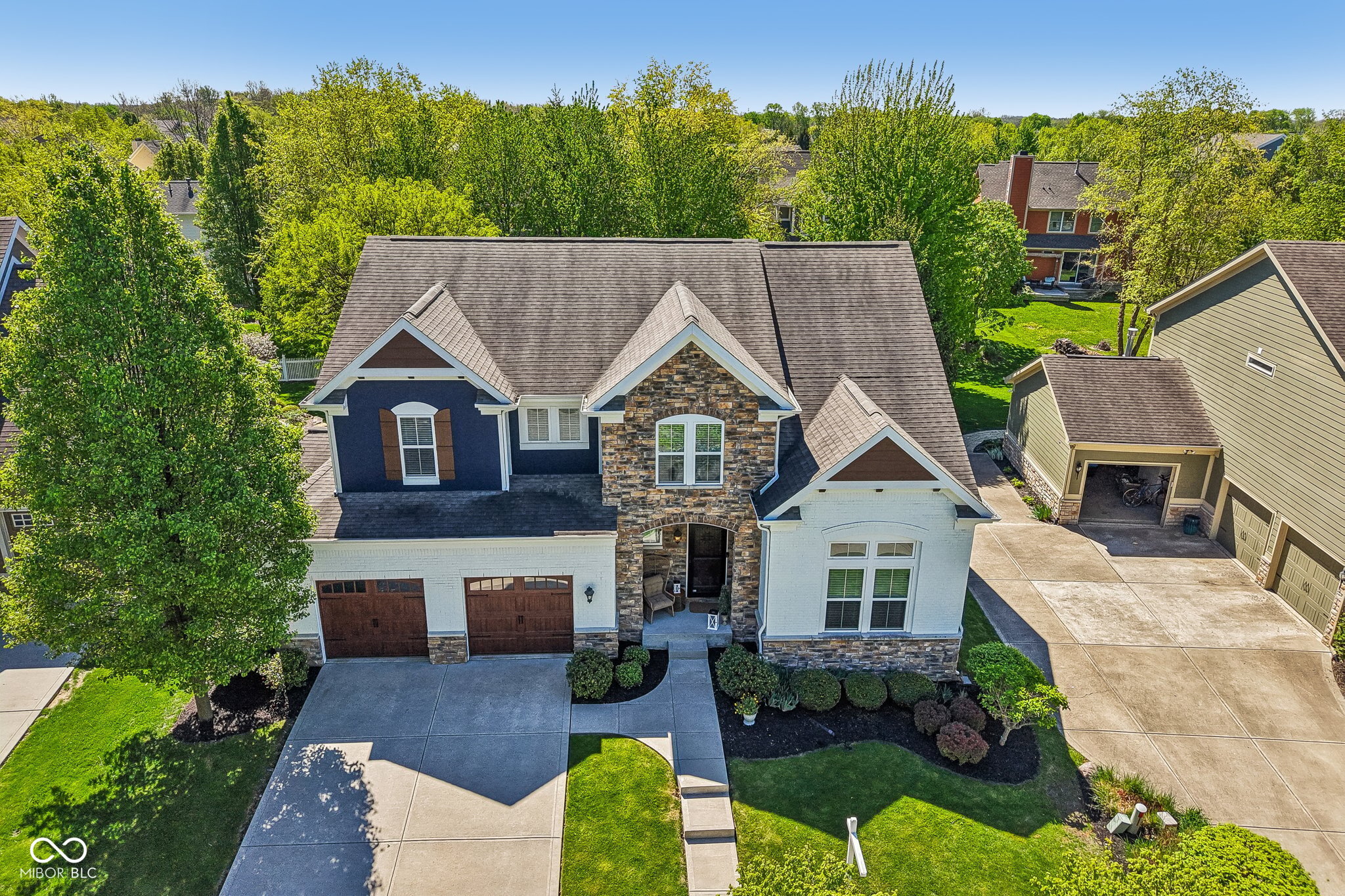 Aerial view of a two-story home with a stone facade, two-car garage, and landscaped front yard.