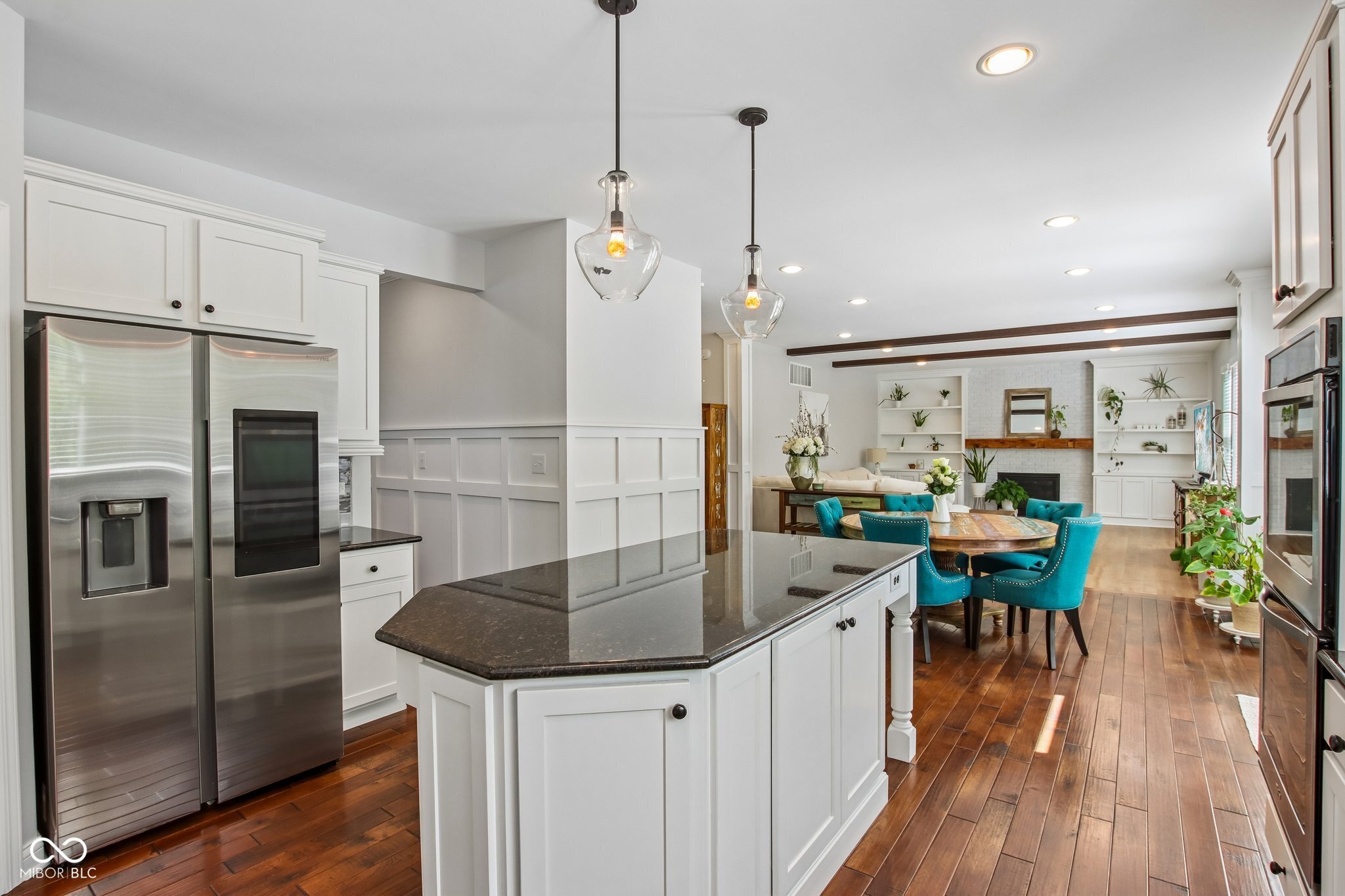 Open-plan kitchen with a large dark island, stainless steel appliances, and teal dining chairs.
