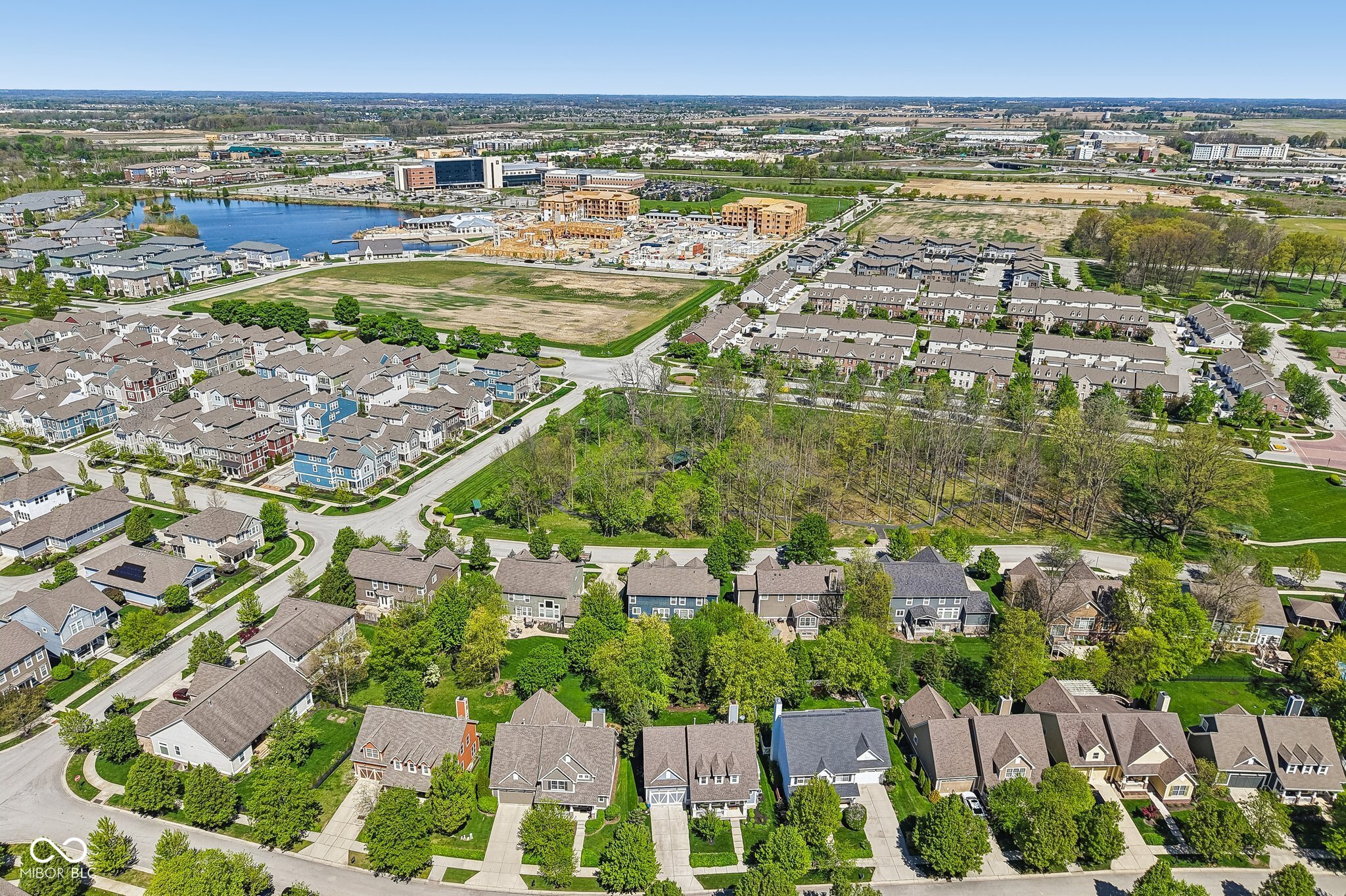 Aerial view of a suburban neighborhood with a wooded greenbelt, pond, and nearby construction.