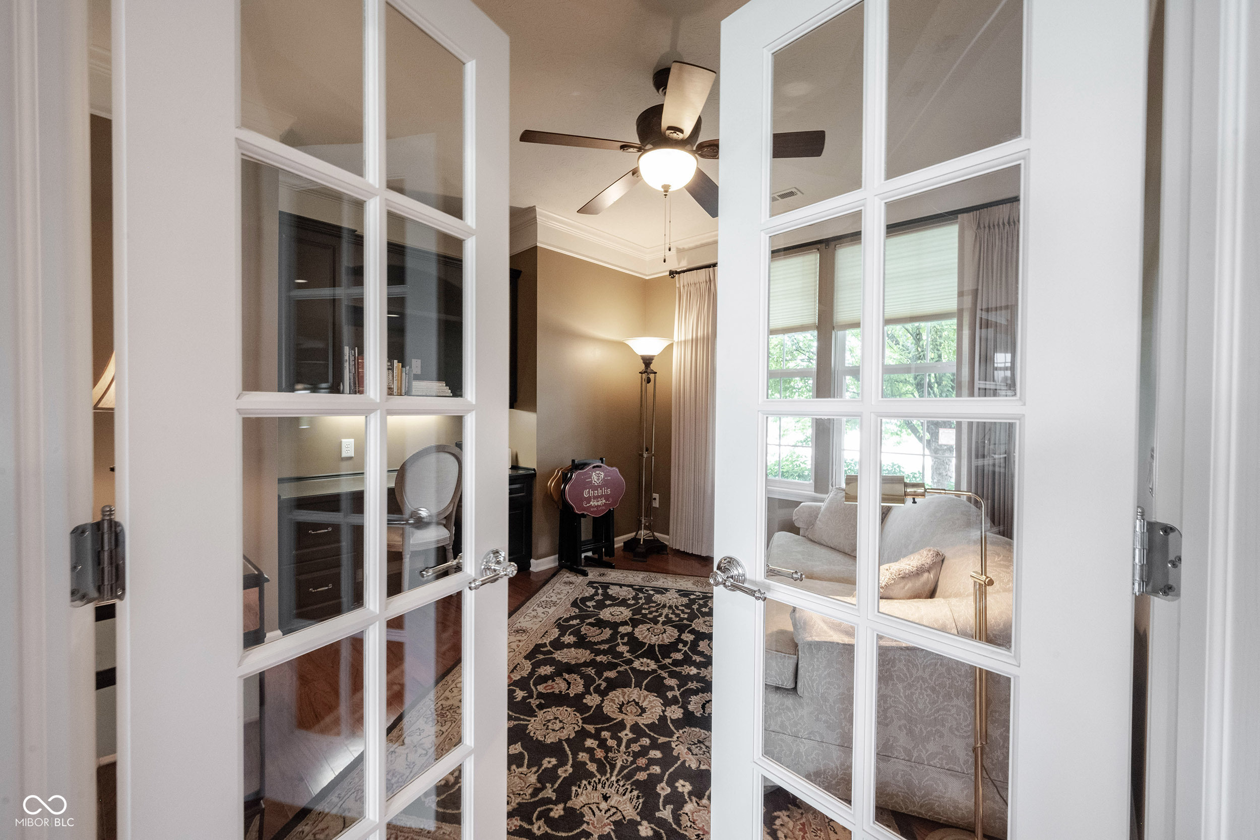 Furnished sitting room seen through French doors, with a patterned rug, pale sofa, and ceiling fan.