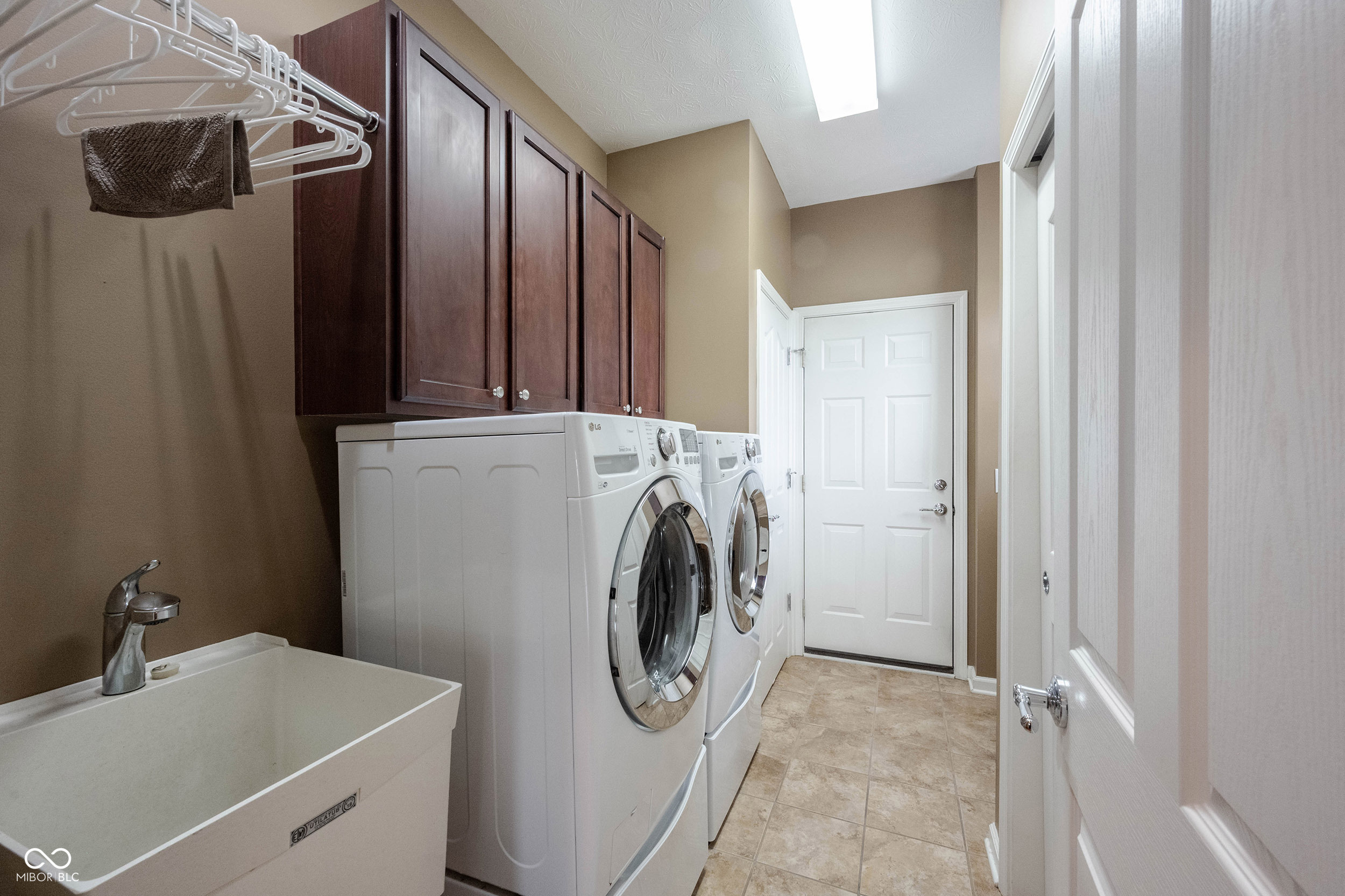 Laundry room with front-loading washer and dryer, dark wood cabinets, and a utility sink.