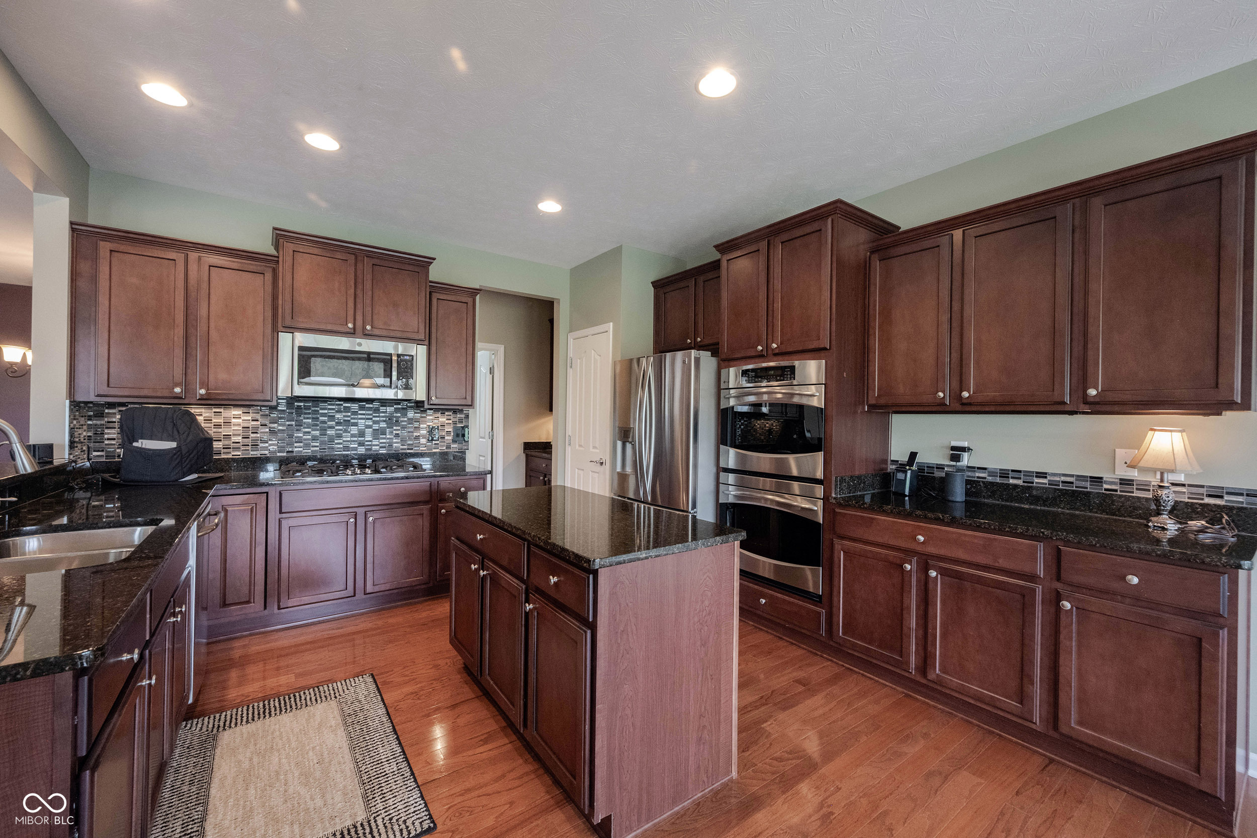 Kitchen with dark cherry cabinets, black granite counters, a central island, and stainless steel appliances.
