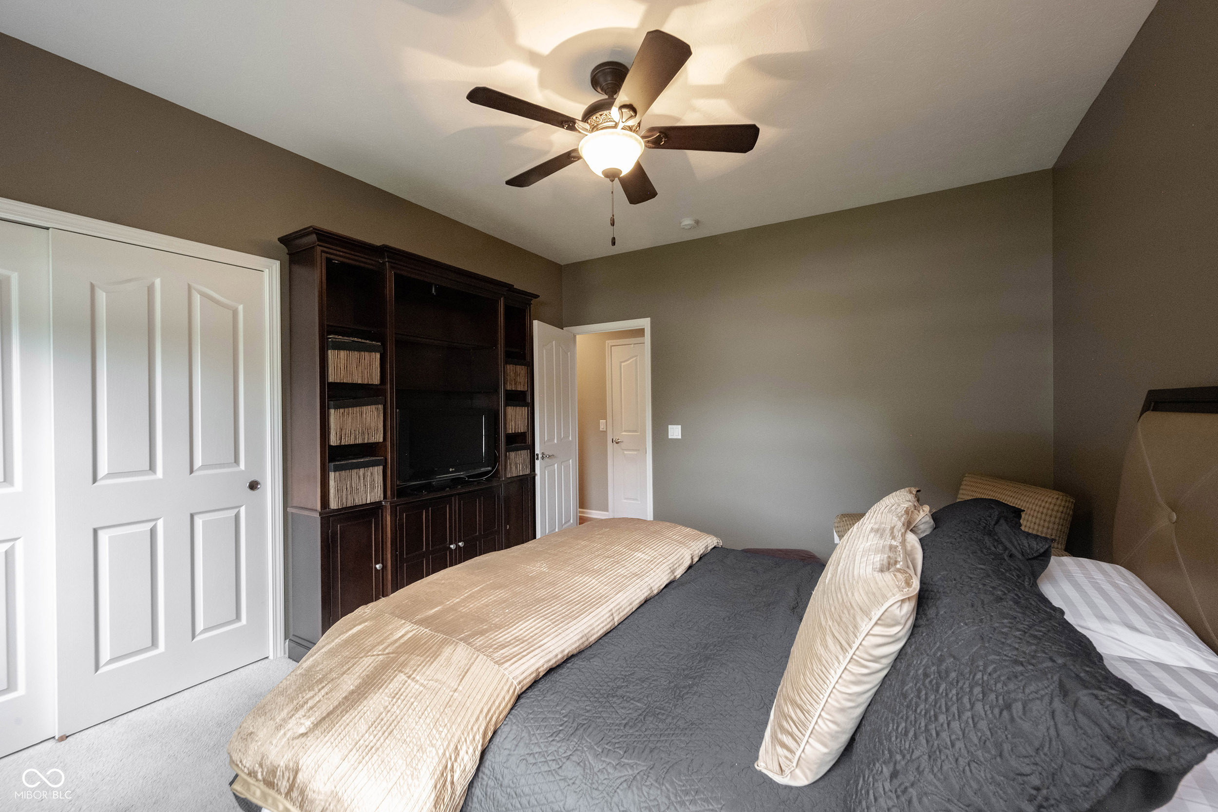 Bedroom with a large gray-and-cream bed and dark built-in media cabinetry.