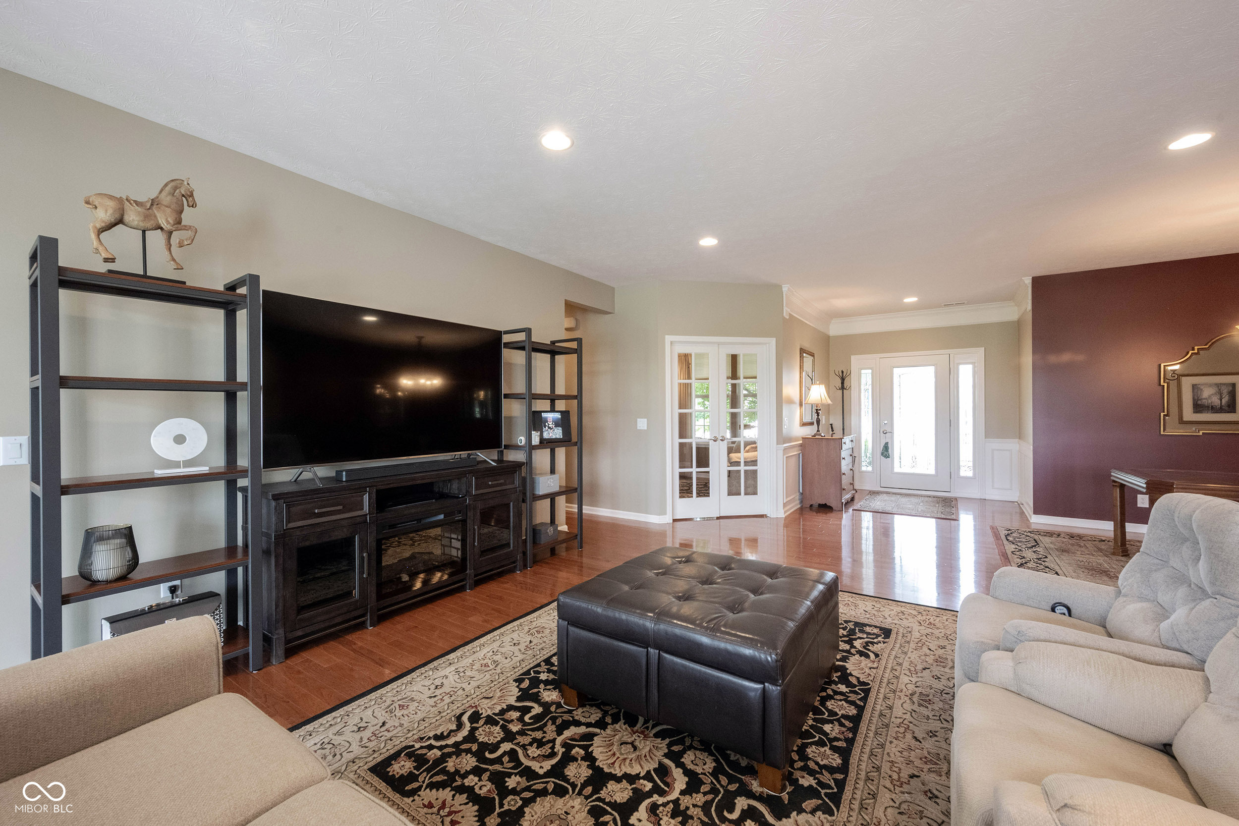 Living room with a large television, cream sofas, patterned rug, and French doors.