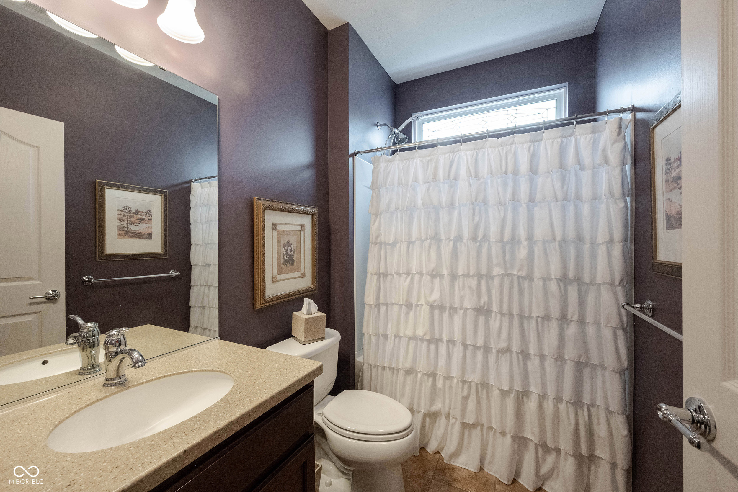 Bathroom with a beige double-sink vanity, dark plum walls, and a white ruffled shower curtain.