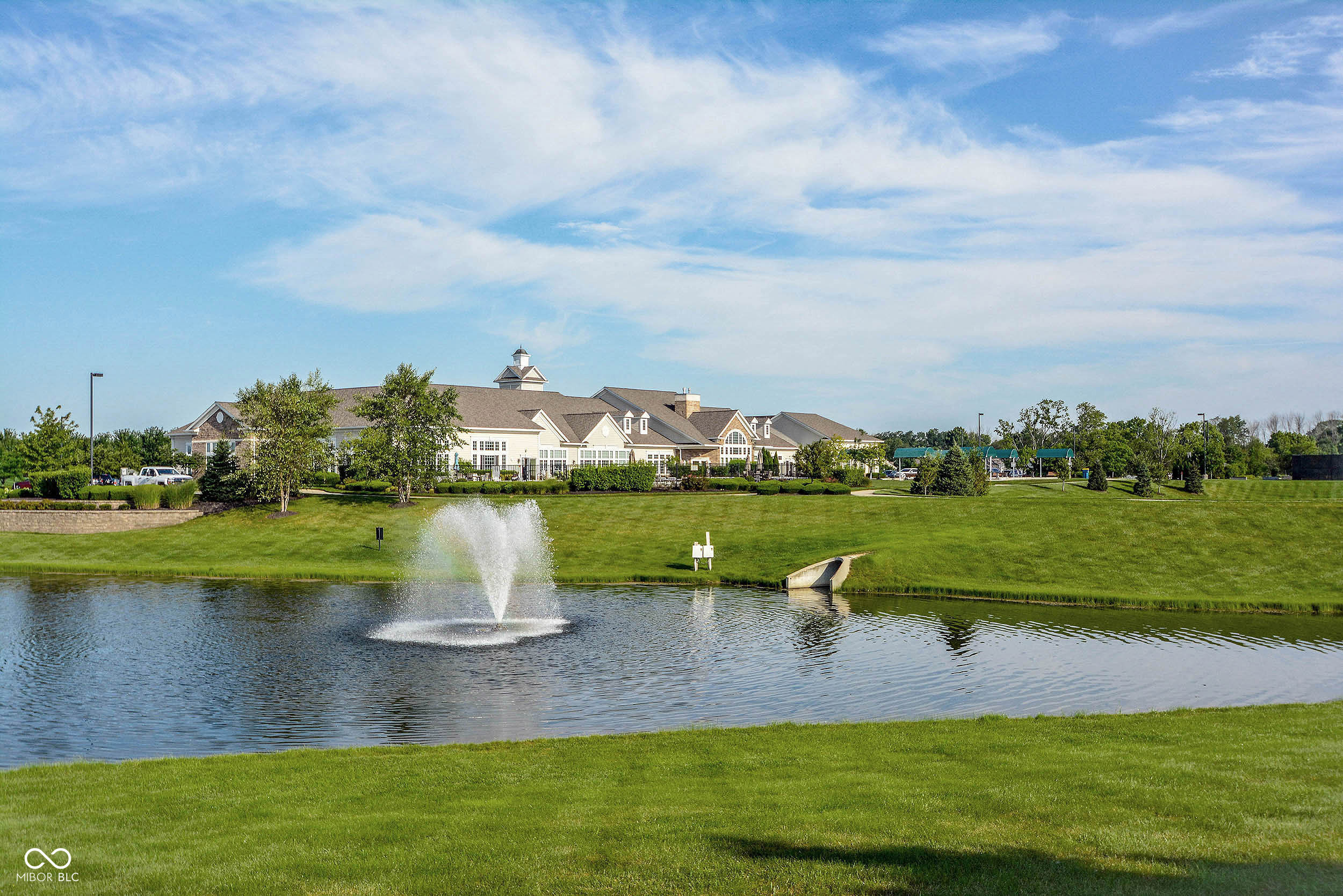 Community building beside a landscaped pond with a fountain spraying in the foreground.