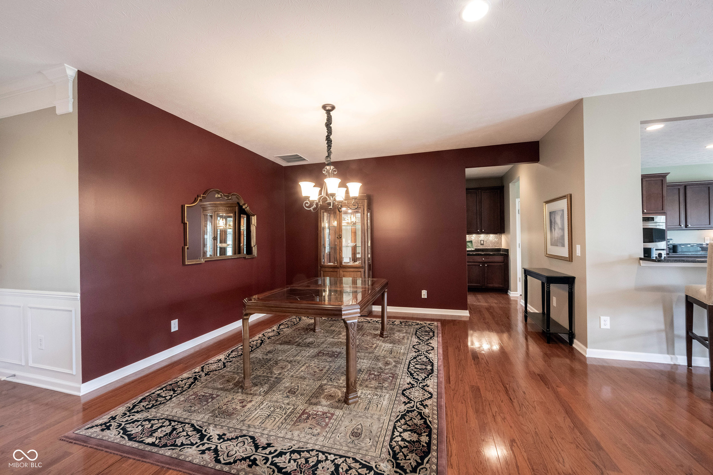 Dining room with burgundy walls, glass-top table, chandelier, and patterned rug.