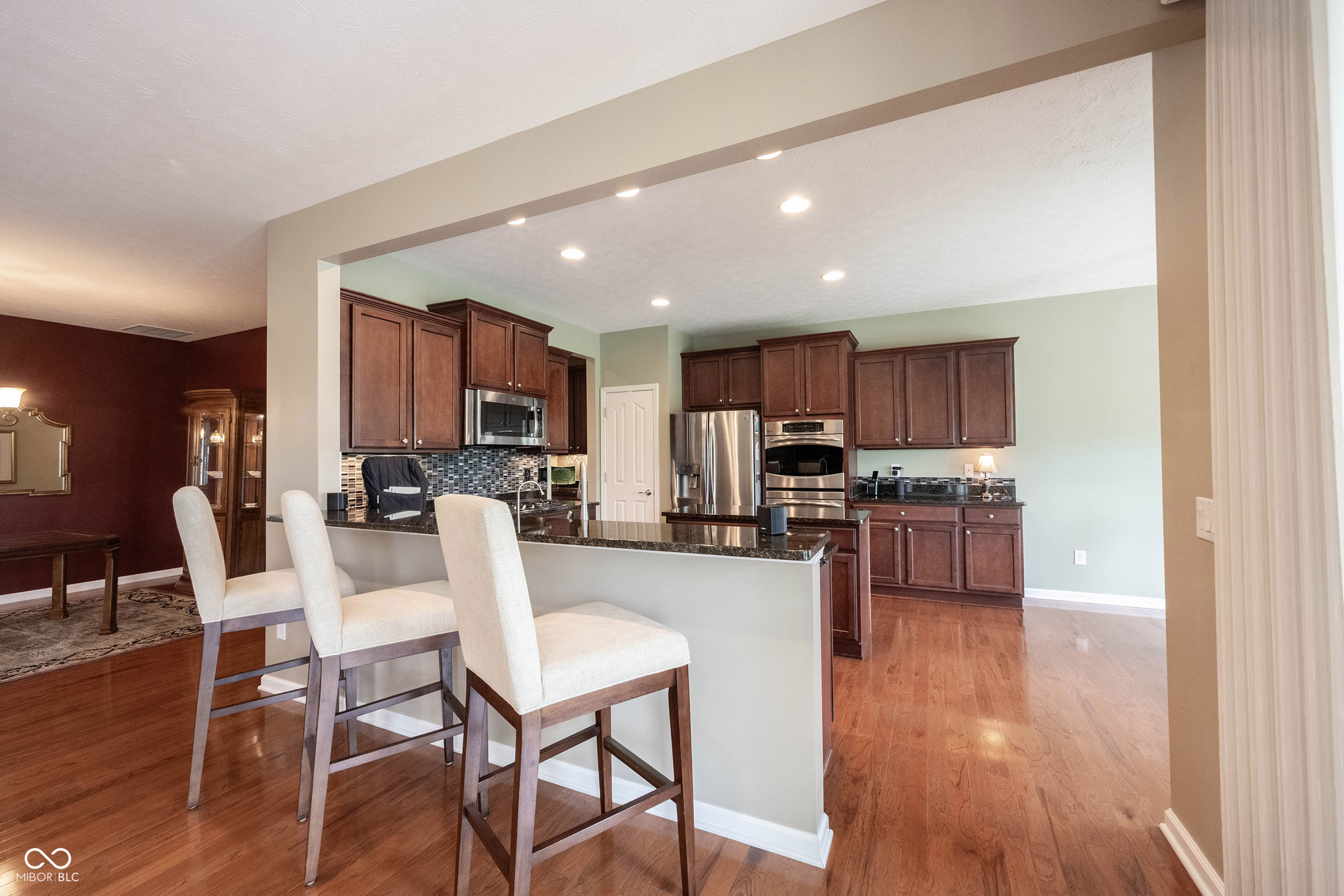 Kitchen with dark wood cabinets, stainless appliances, and a granite island with three upholstered chairs.