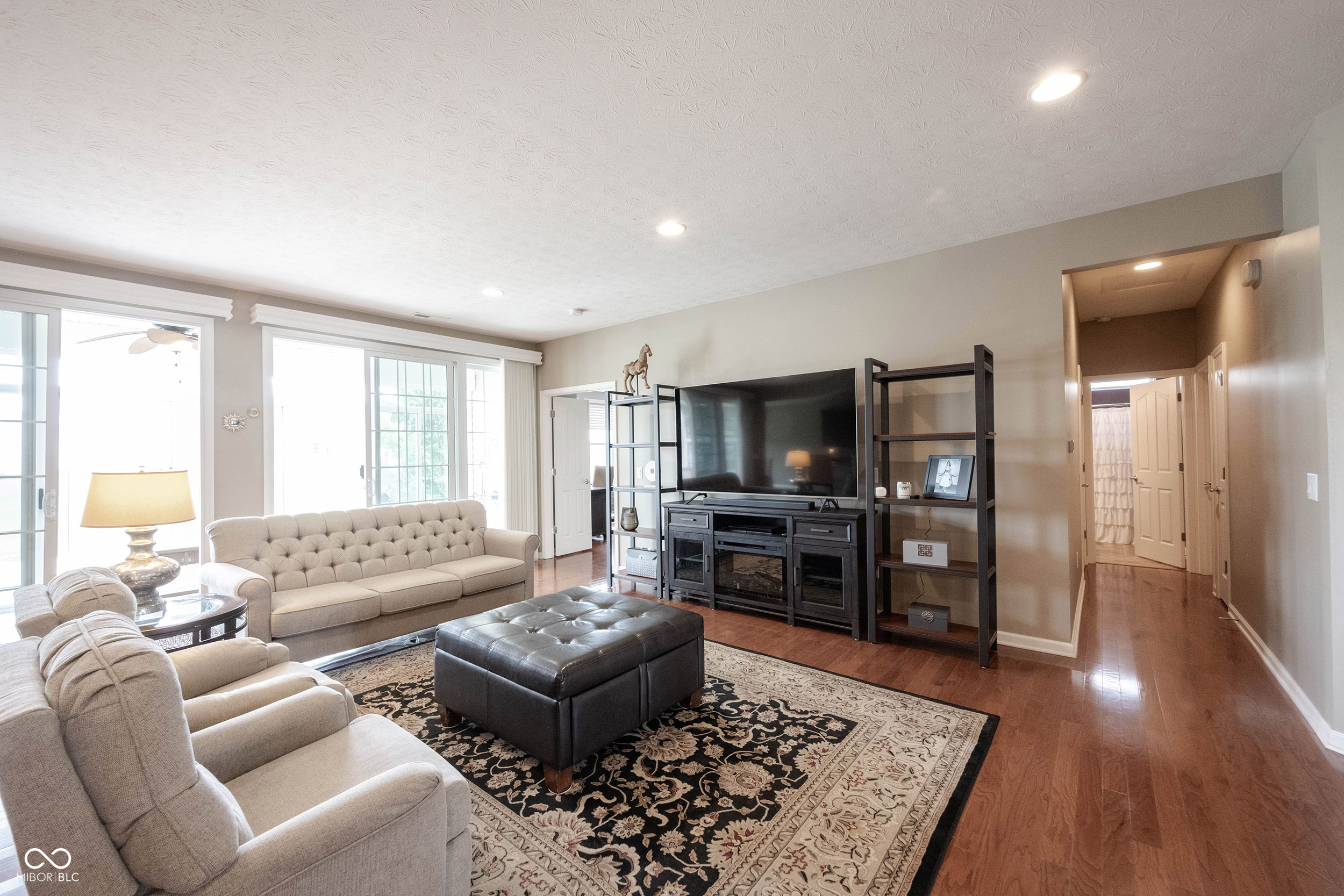 Furnished living room with beige tufted sofas, a black leather ottoman, and a large television.