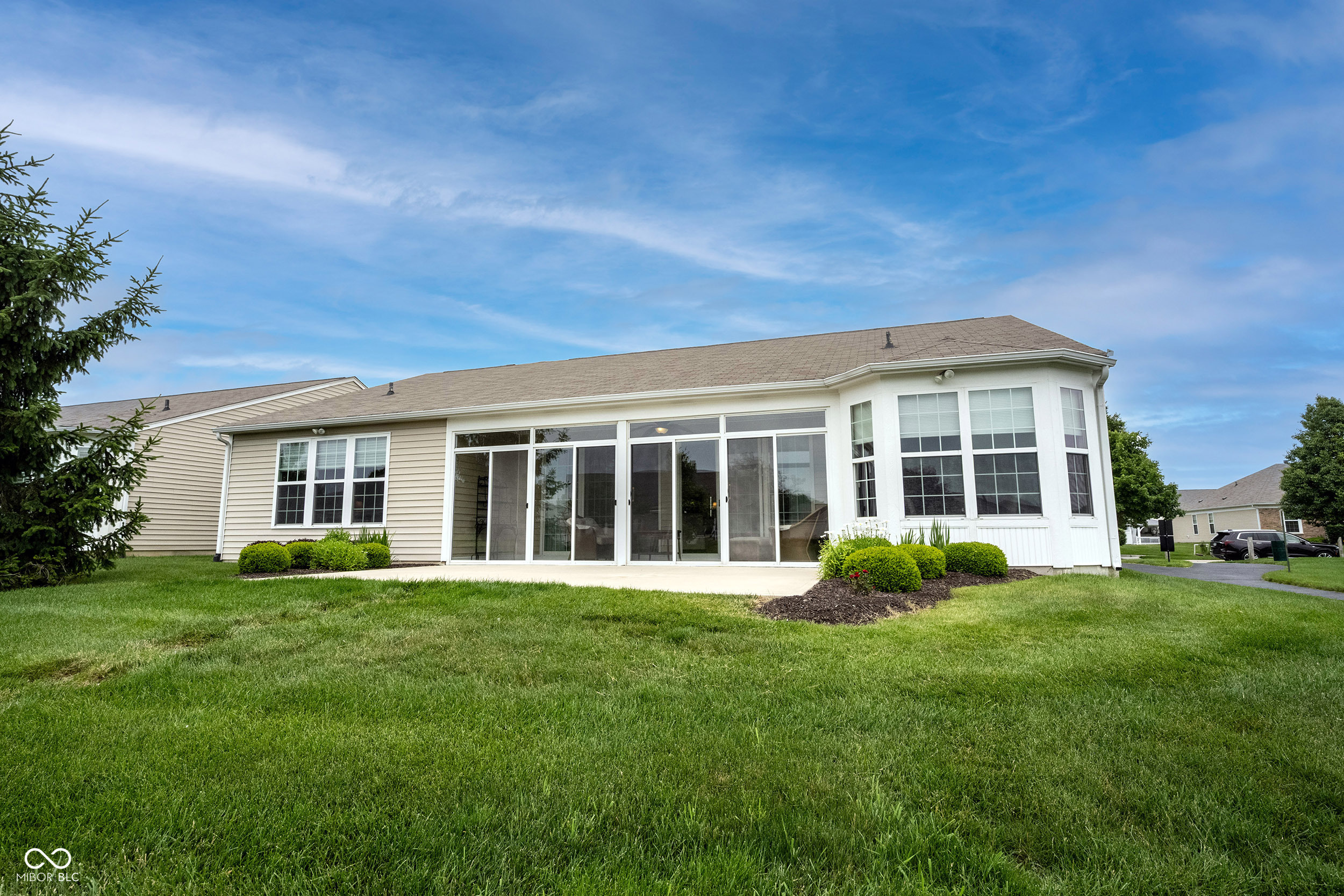 House rear with a white windowed sunroom, landscaped shrubs, and a broad lawn.