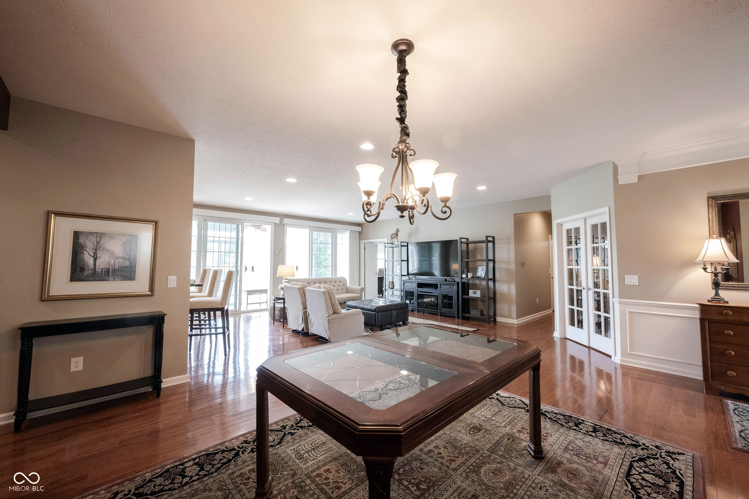 Furnished living room with a glass-top coffee table, patterned rug, chandelier, and TV entertainment unit.