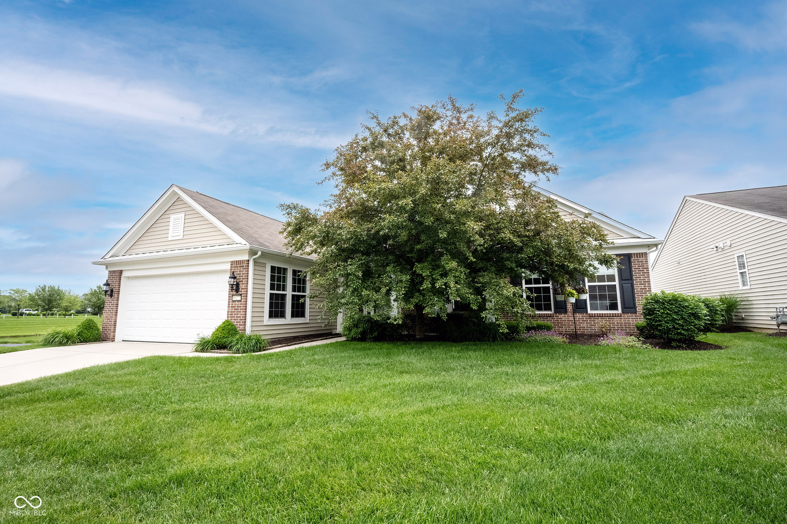 Home exterior with an attached garage, brick accents, and a large tree in the front yard.